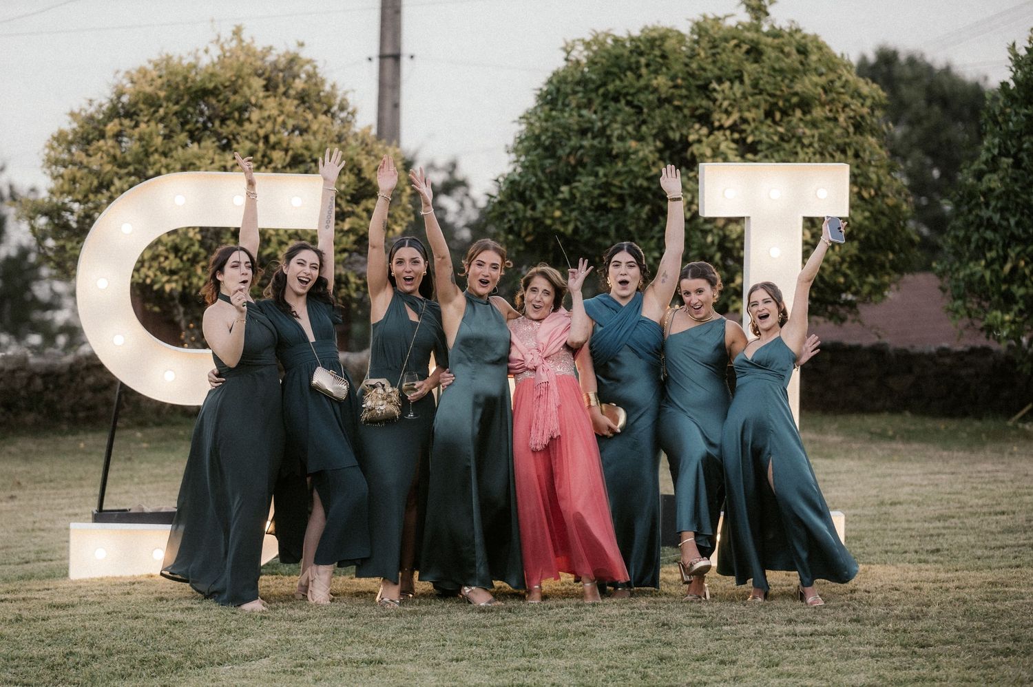 Wedding party in coordinated blue dresses poses together on lawn with decorative letters in background.
