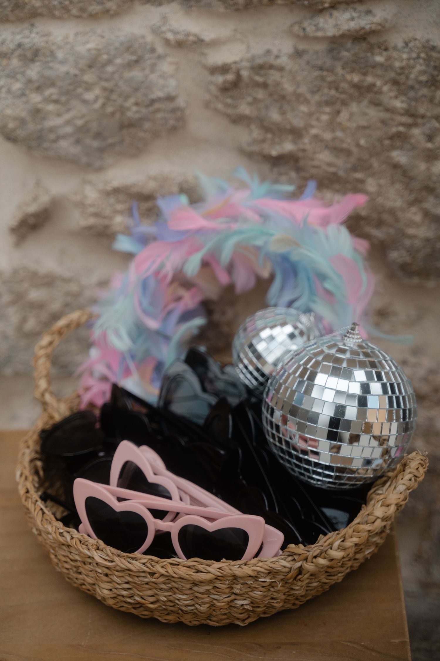 A disco ball and colorful party accessories arranged in a woven basket with pink and blue feathers.