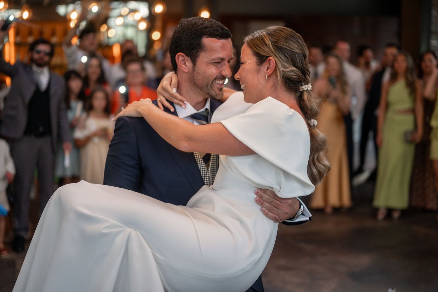 Couple dancing intimately on their wedding day surrounded by guests in an elegantly lit indoor venue.