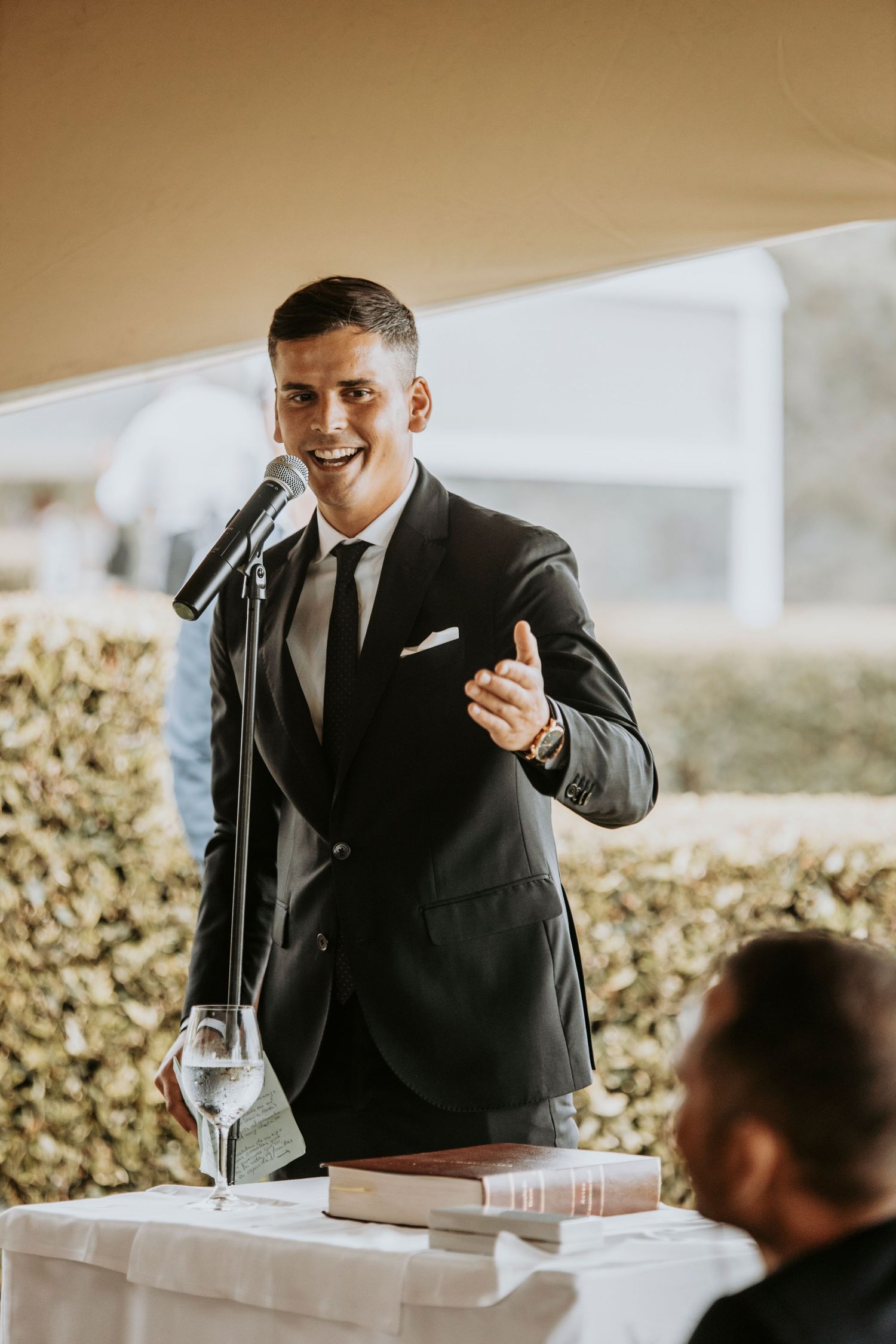 Someone in a dark suit gives a heartfelt speech at an elegant wedding reception venue.