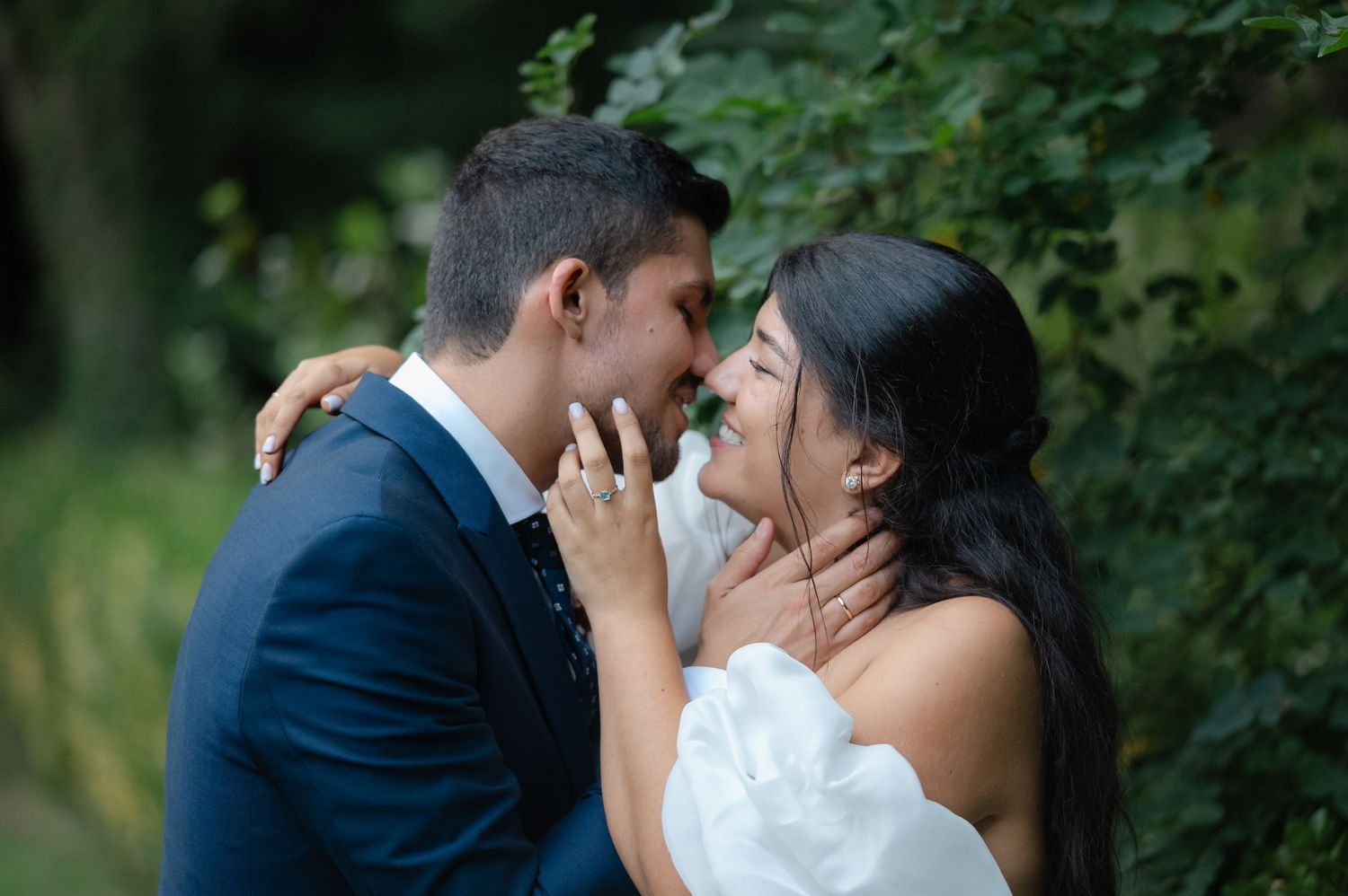 A romantic couple shares an intimate moment in a garden setting wearing wedding attire.