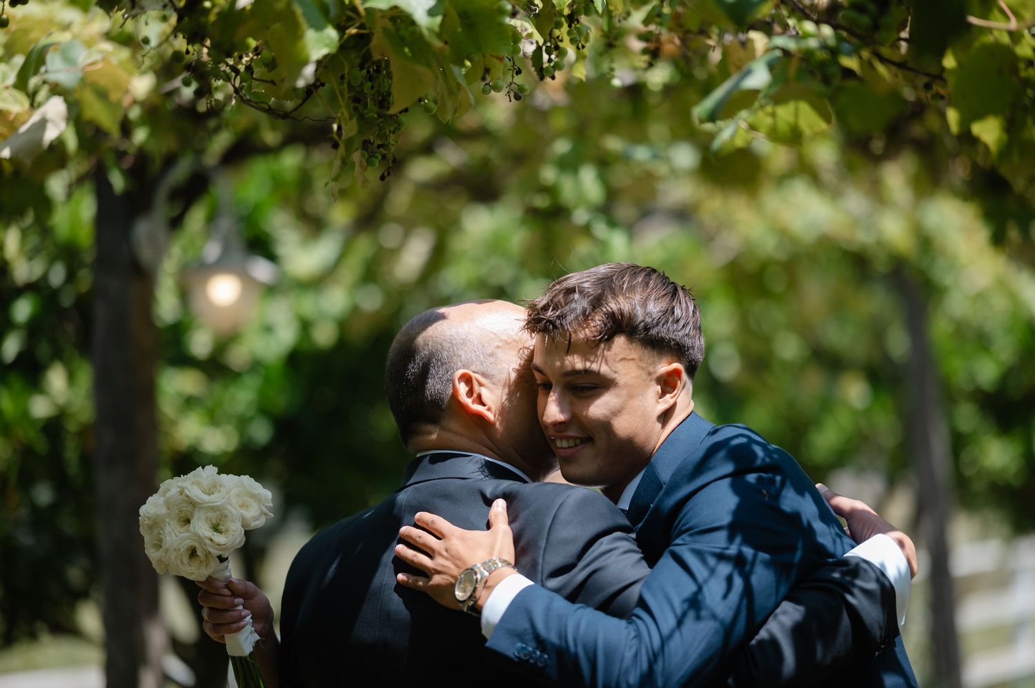 A romantic outdoor wedding ceremony with couples embracing under lush green trees.