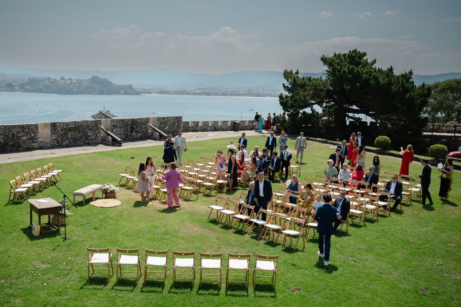 Outdoor wedding ceremony setup with white chairs arranged on a grassy hillside overlooking the ocean.