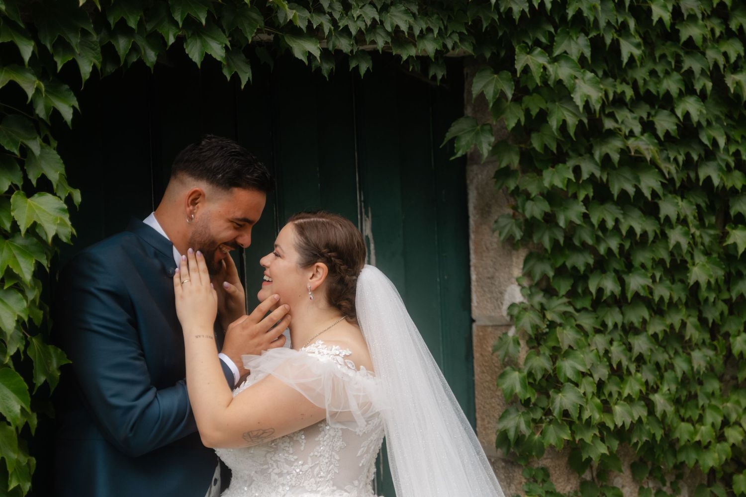 A couple shares a romantic moment in front of an ivy-covered wall during their wedding celebration.