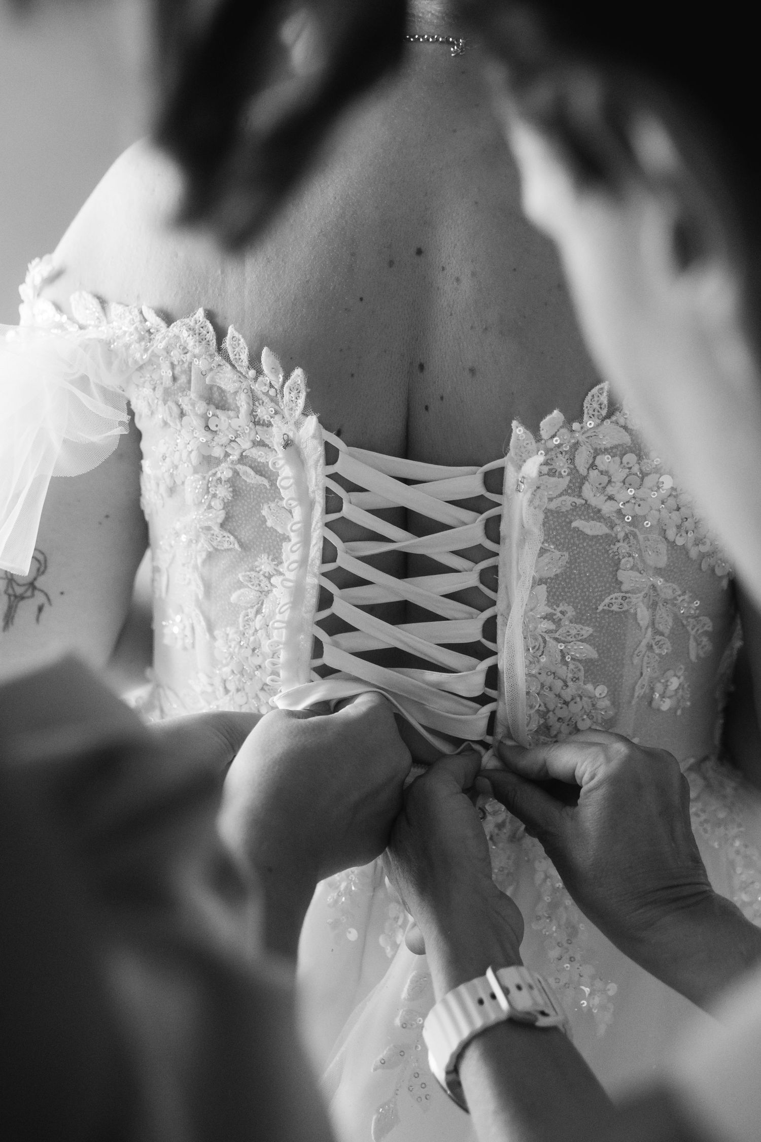Close-up detail of corset lacing on a white lace wedding dress being tied.