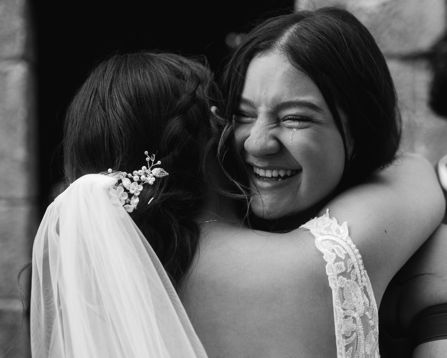 An intimate black and white portrait capturing joyful laughter between wedding attendees.