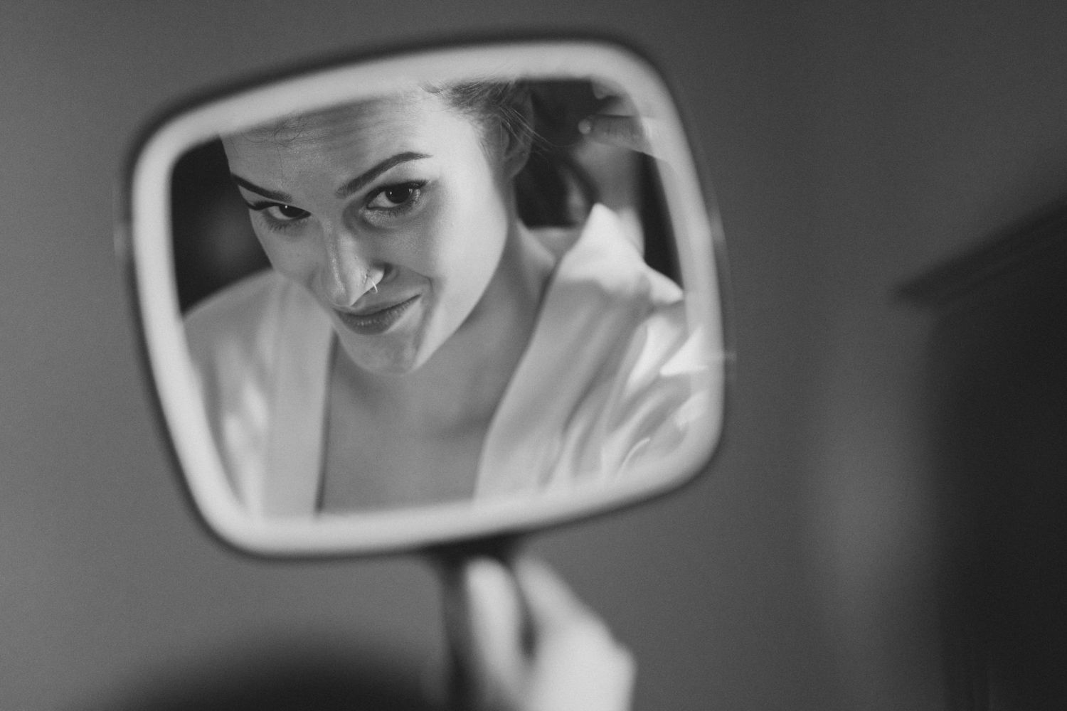 Black and white artistic reflection of a person getting ready in a car side mirror.