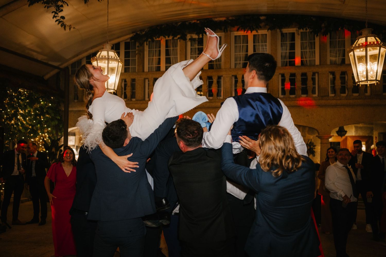 Wedding guests dance and celebrate under warm lantern lighting in an elegant indoor venue.