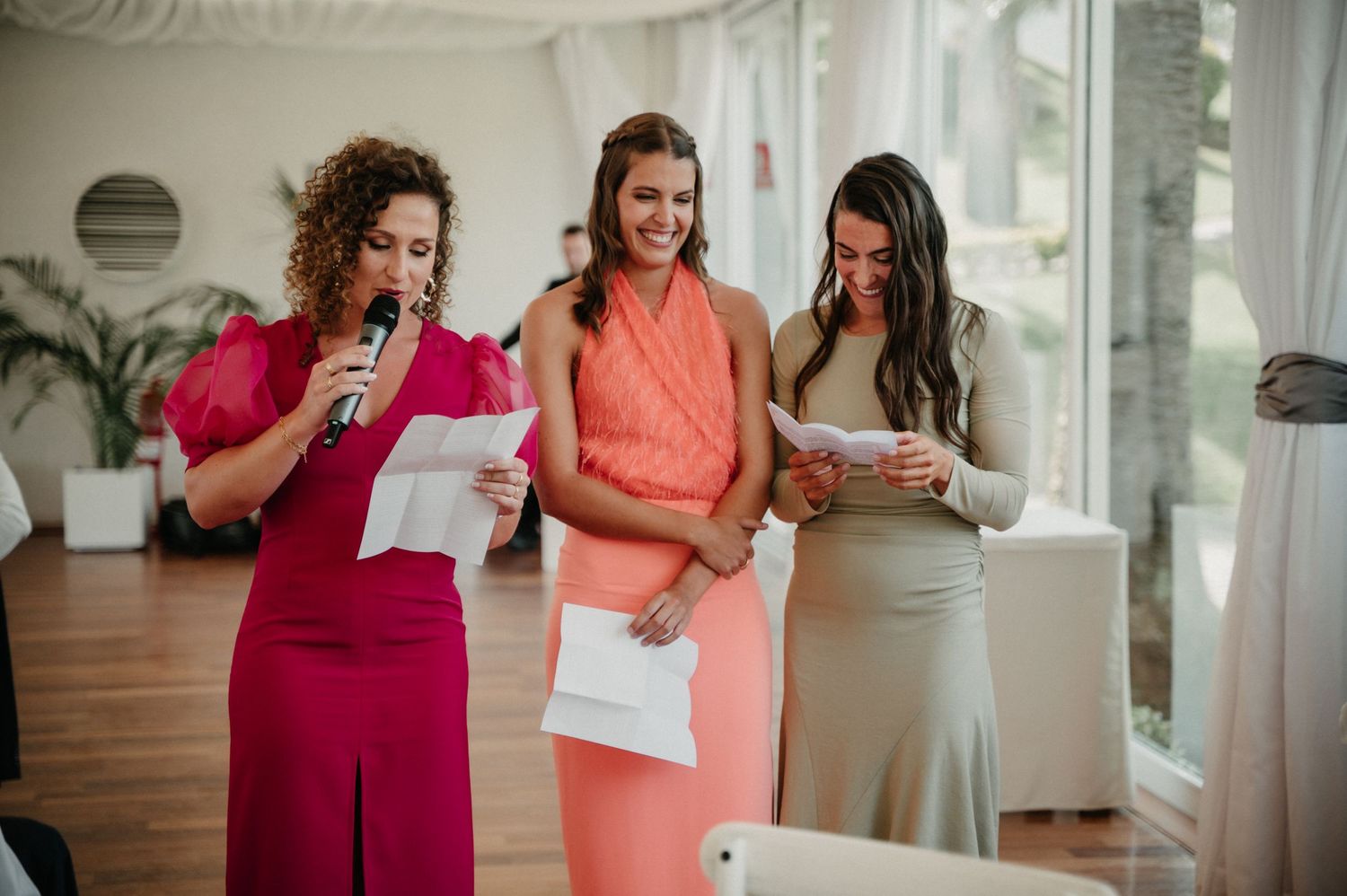 Wedding party members in coral and burgundy dresses share joyful moments during celebration preparations.