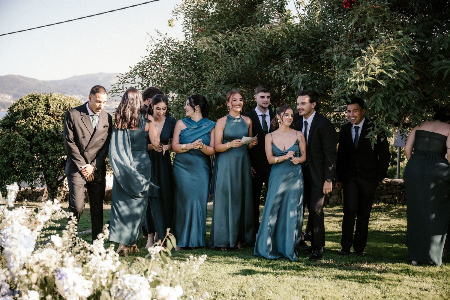 Wedding party wearing dusty blue dresses and suits poses together in an outdoor garden setting.