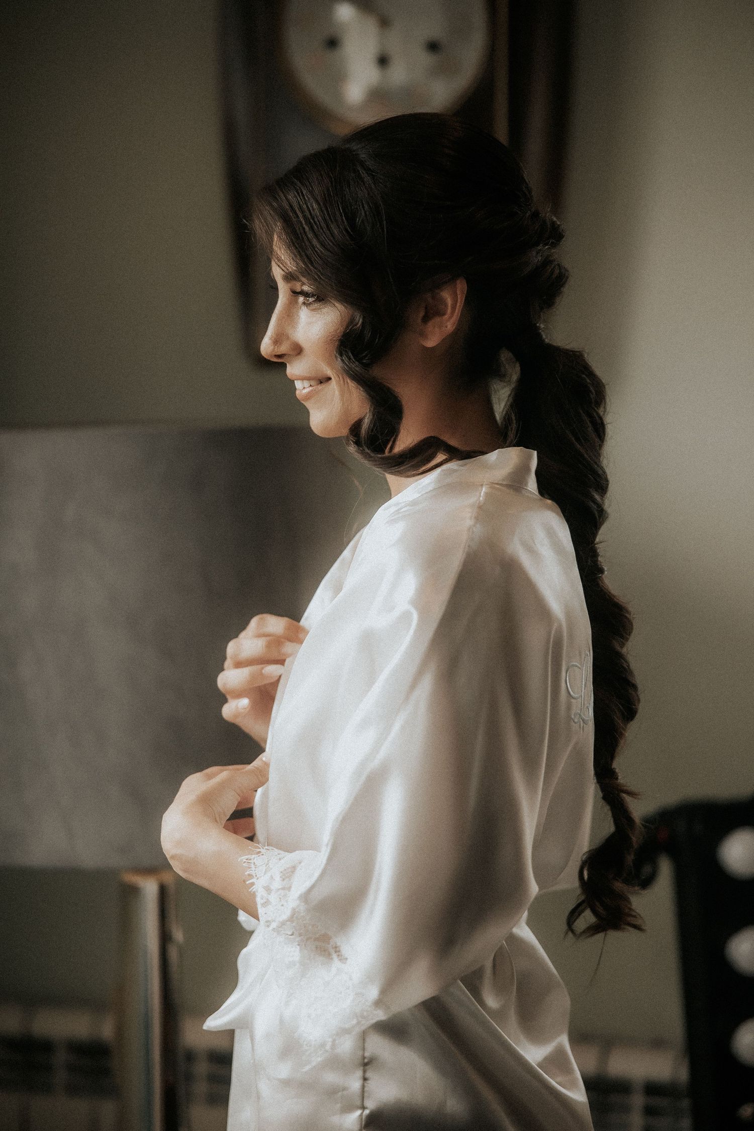 Side profile of someone wearing a white silk robe while getting ready, with long dark wavy hair in a ponytail.