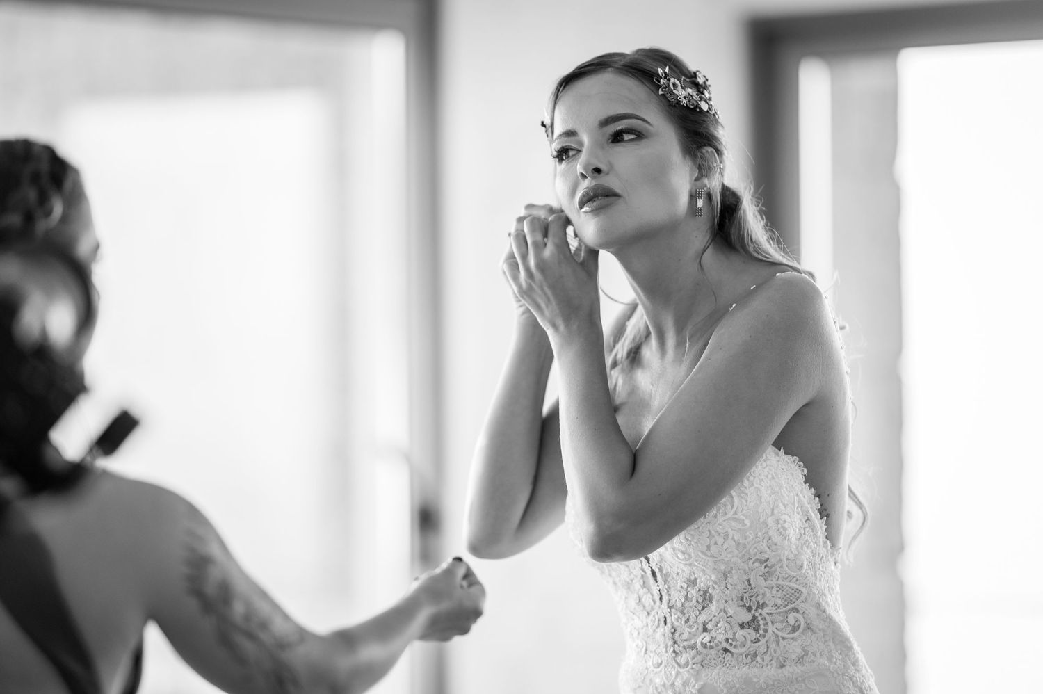 A bride in a white wedding dress applies lipstick while getting ready in a bright sunlit room.