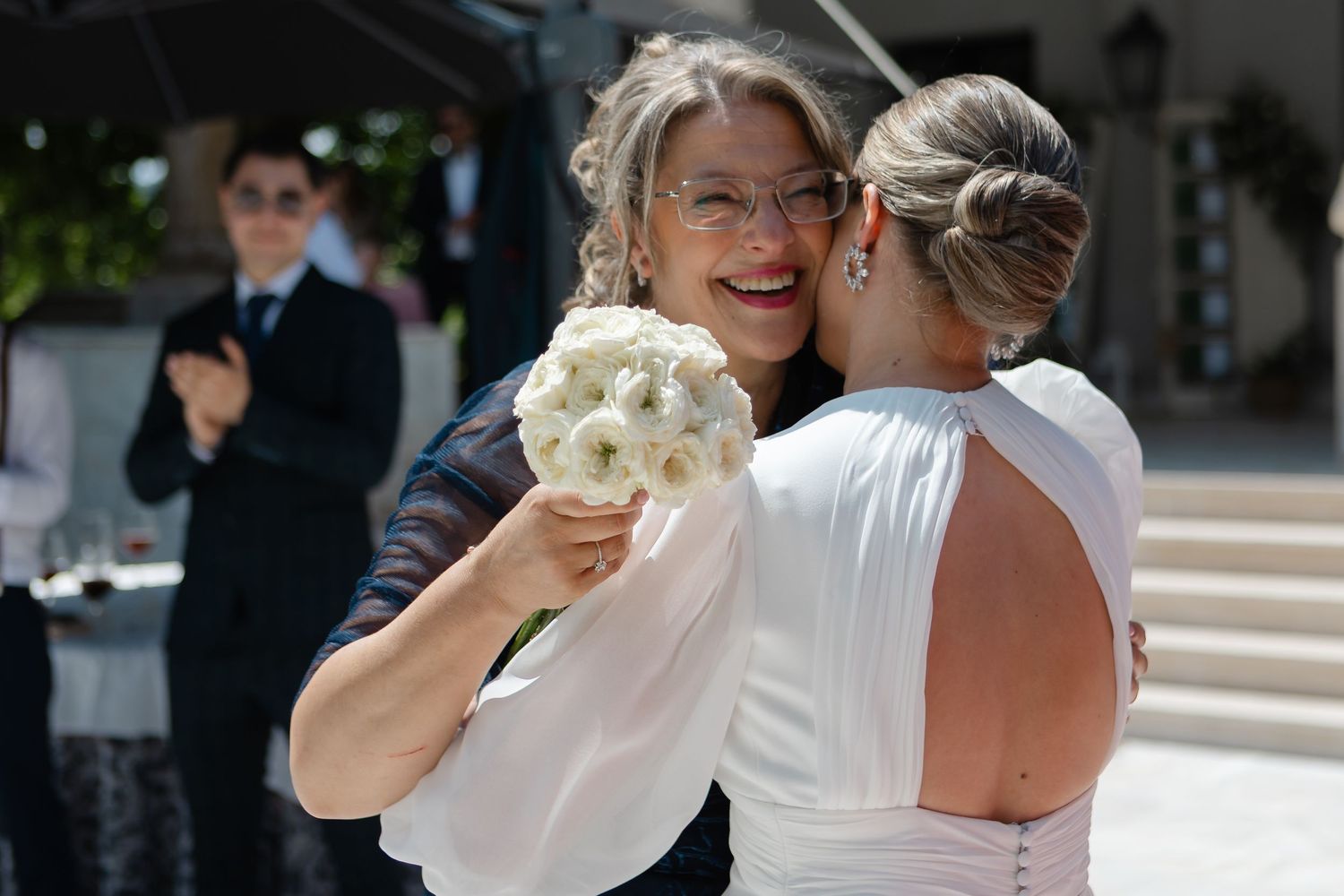A couple shares a tender moment during their wedding dance while guests look on at an outdoor reception.