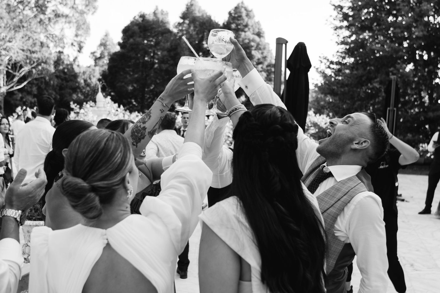 A joyful group raises their champagne glasses in celebration at an outdoor event, captured in black and white.