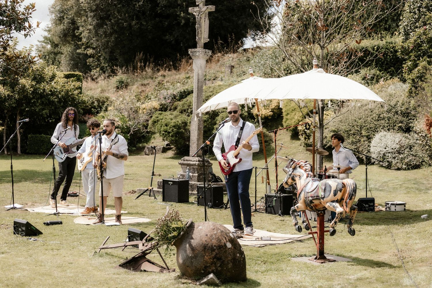 Outdoor wedding celebration with white umbrellas and lounge furniture arranged on a grassy hillside.