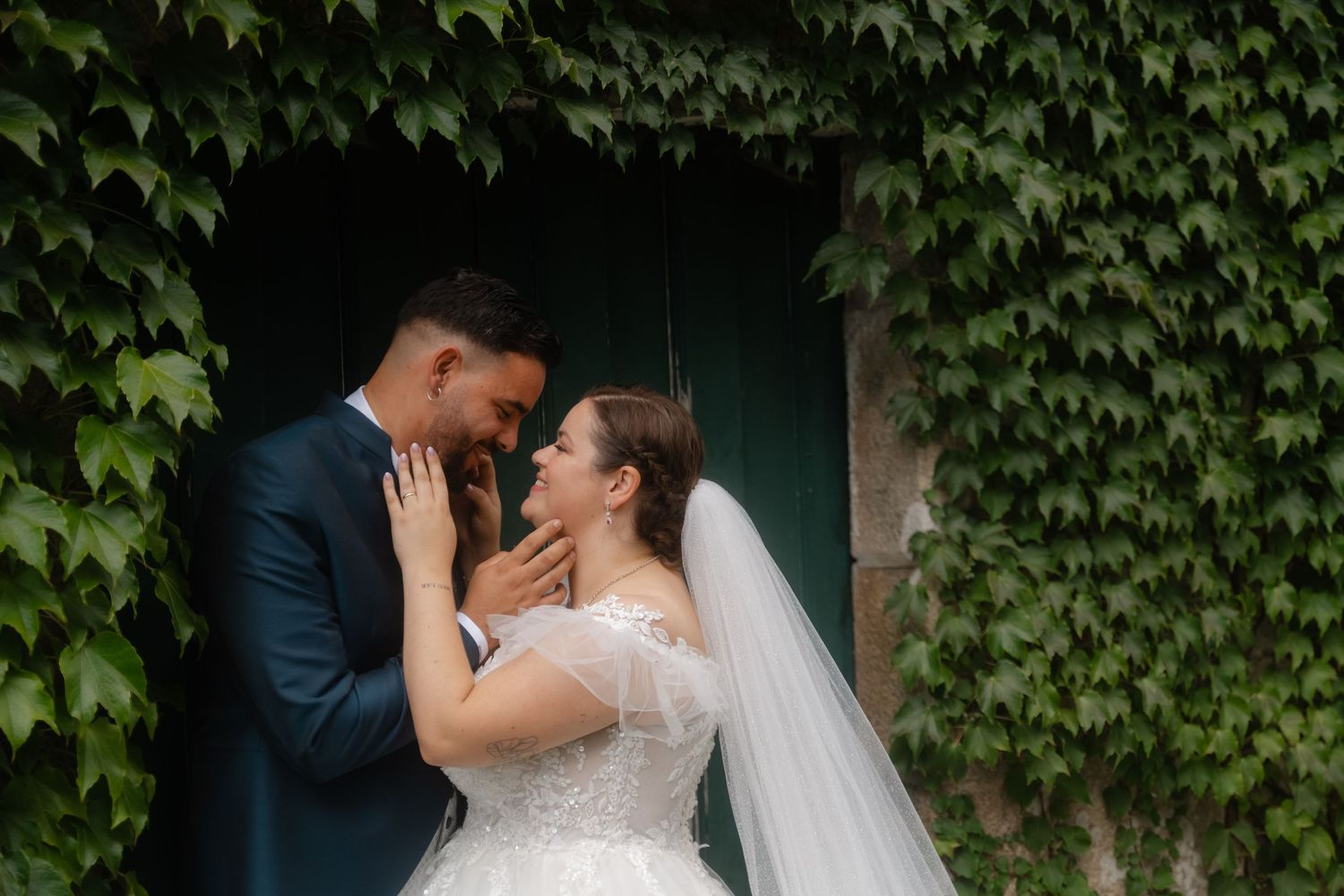 A romantic wedding couple embraces in front of an ivy-covered wall on their special day.