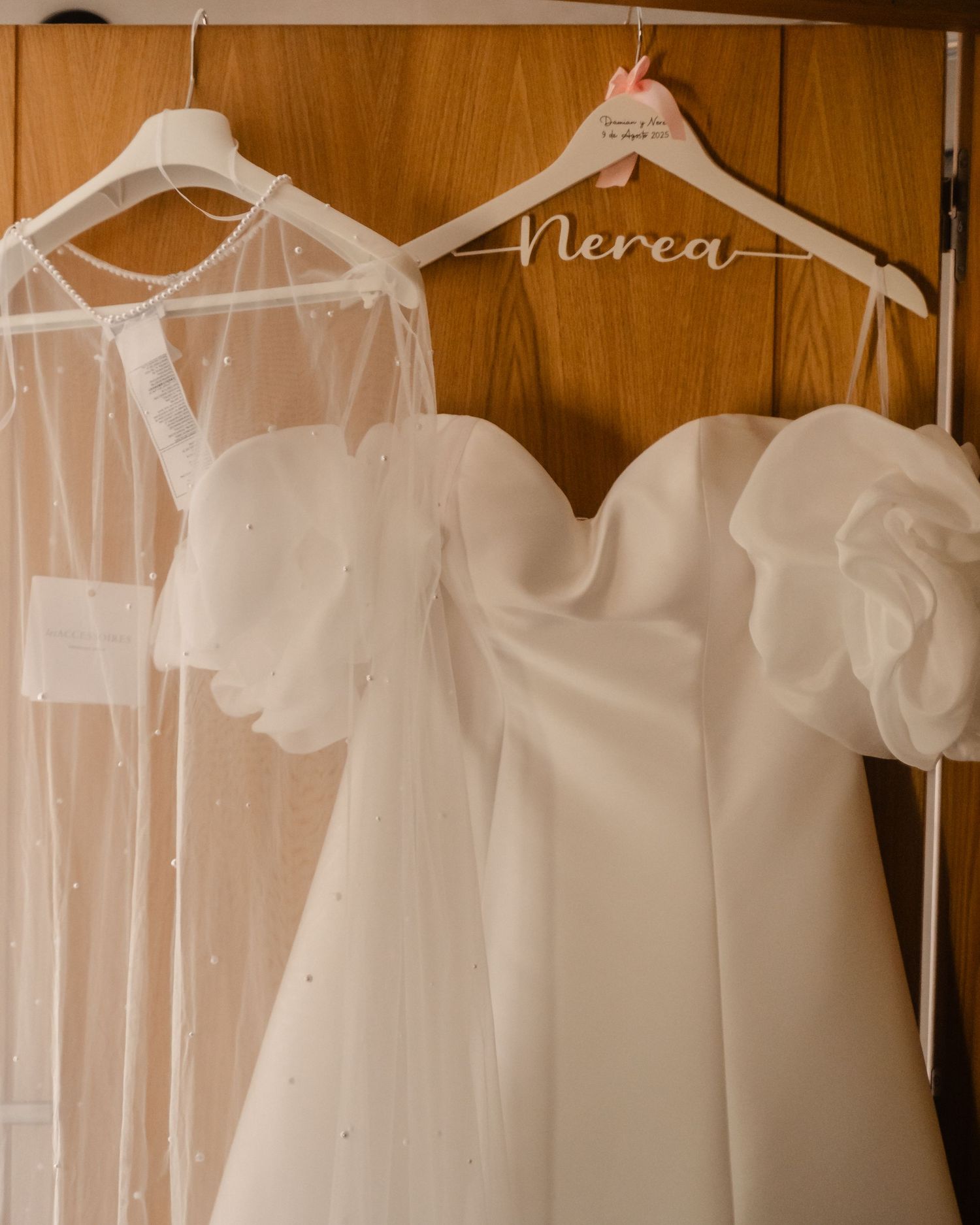 White wedding dress and veil hanging on personalized hangers against a wooden wardrobe.