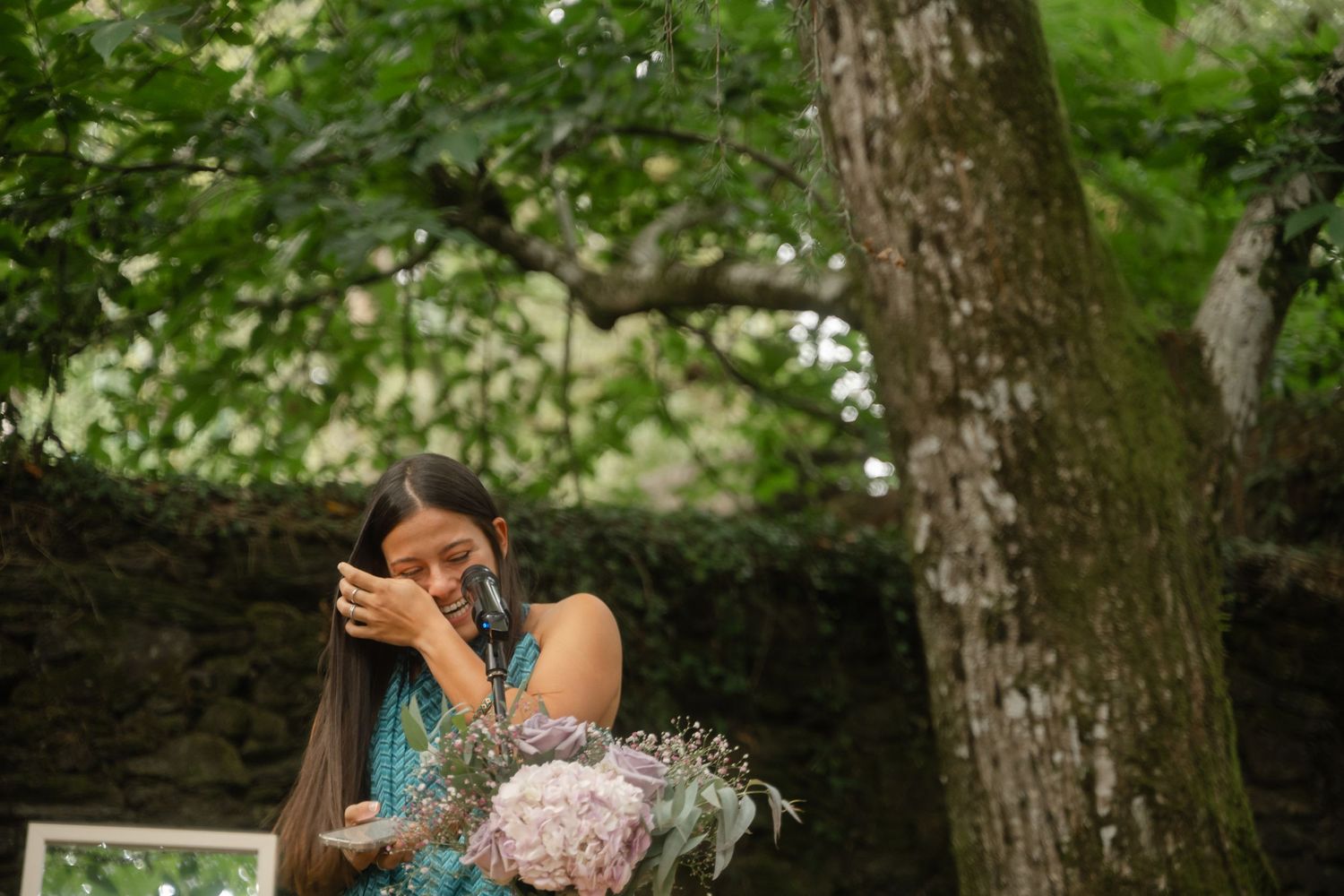 Outdoor wedding celebration with guests gathered among trees in a natural setting.