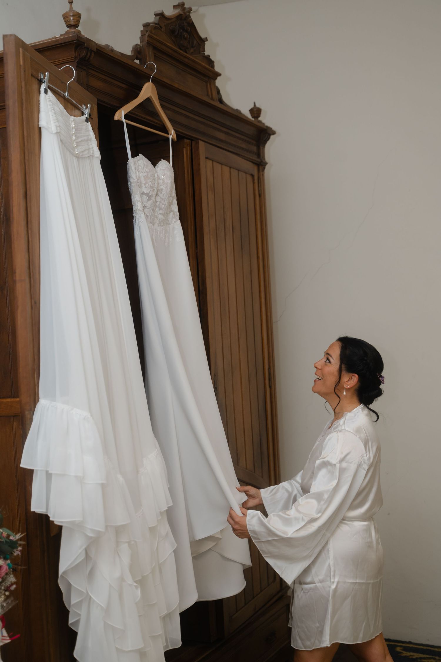 A series of photos showing someone in a white robe looking up at a wedding dress hanging from an ornate wooden wardrobe.