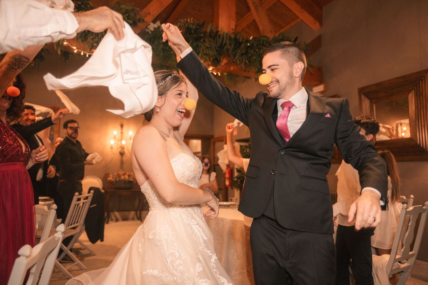 Couples dance together during a wedding reception in a warmly lit rustic venue with wood beams and elegant decor.