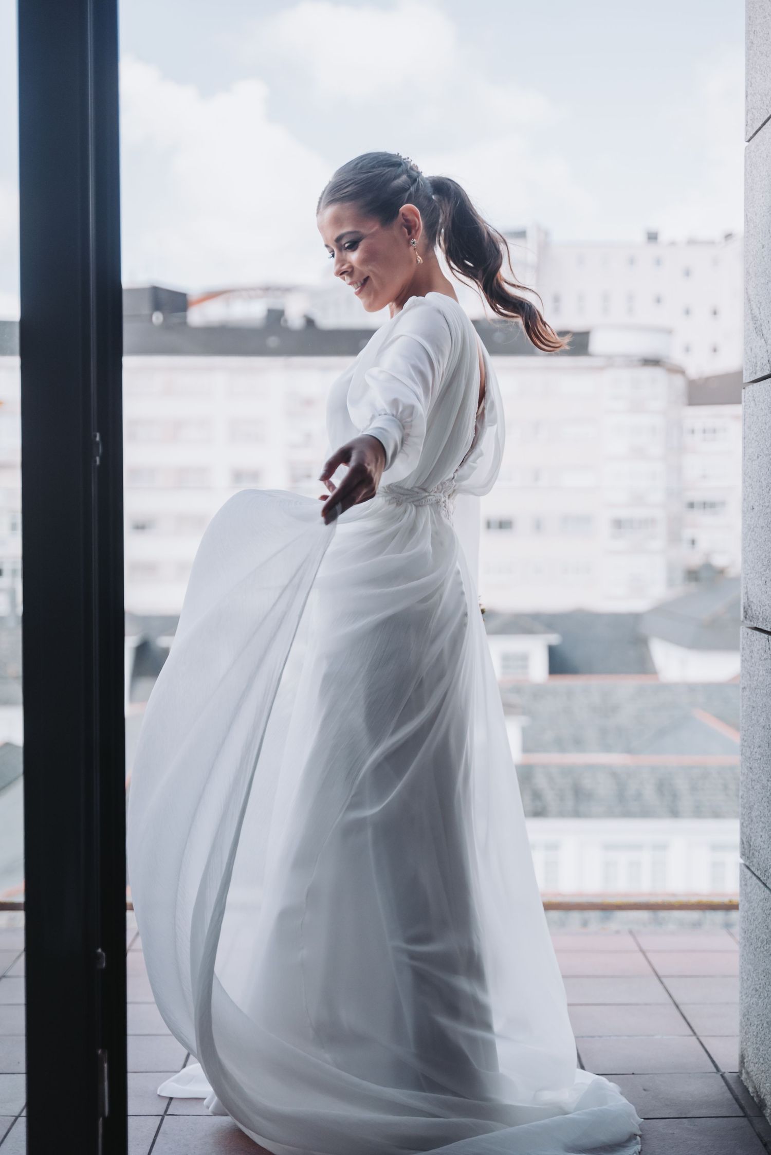 Elegant wedding dress flowing in the breeze on a balcony with city views.