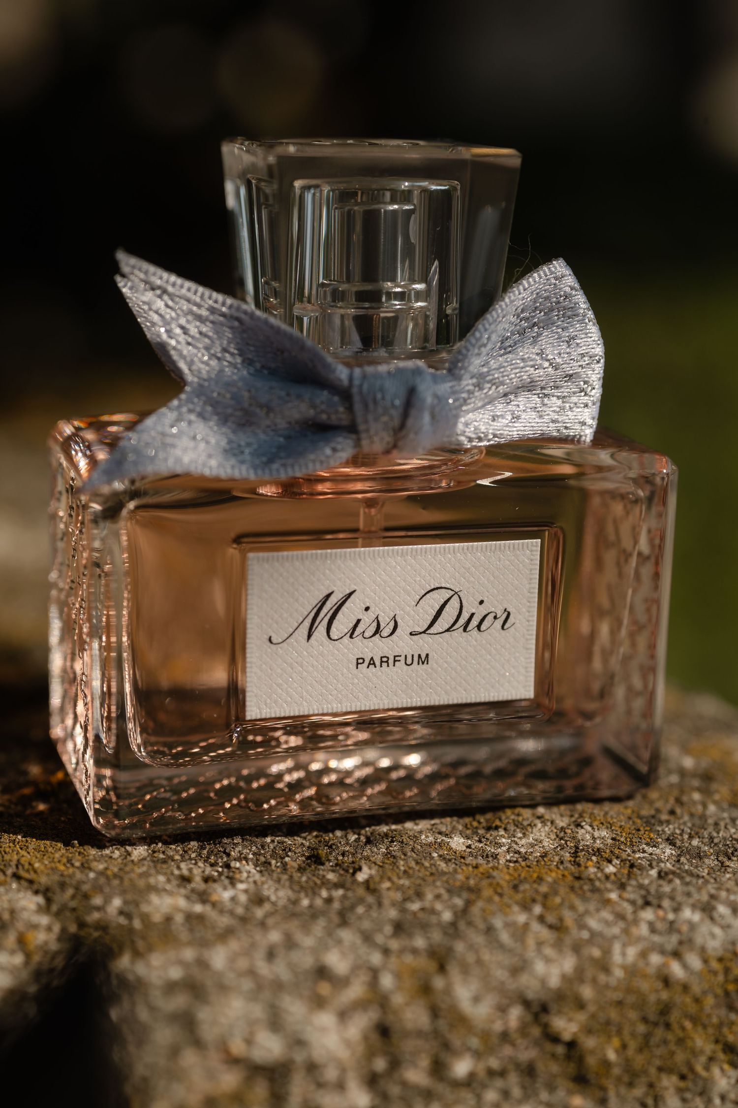 Miss Dior perfume bottle with delicate blue bow photographed on stone surface in natural light.