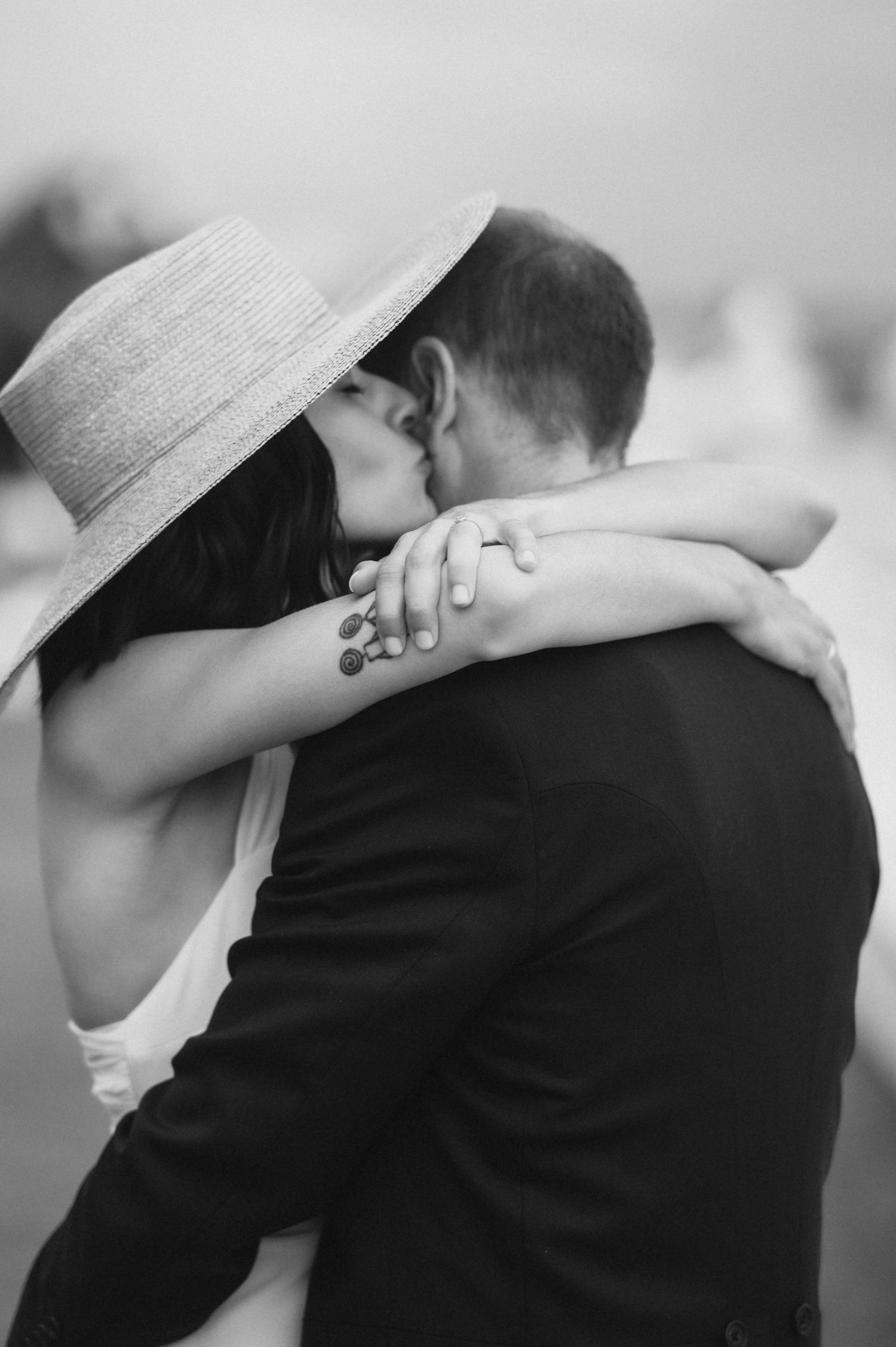 A romantic black and white photo series showing a couple embracing while one wears a wide-brimmed sun hat.