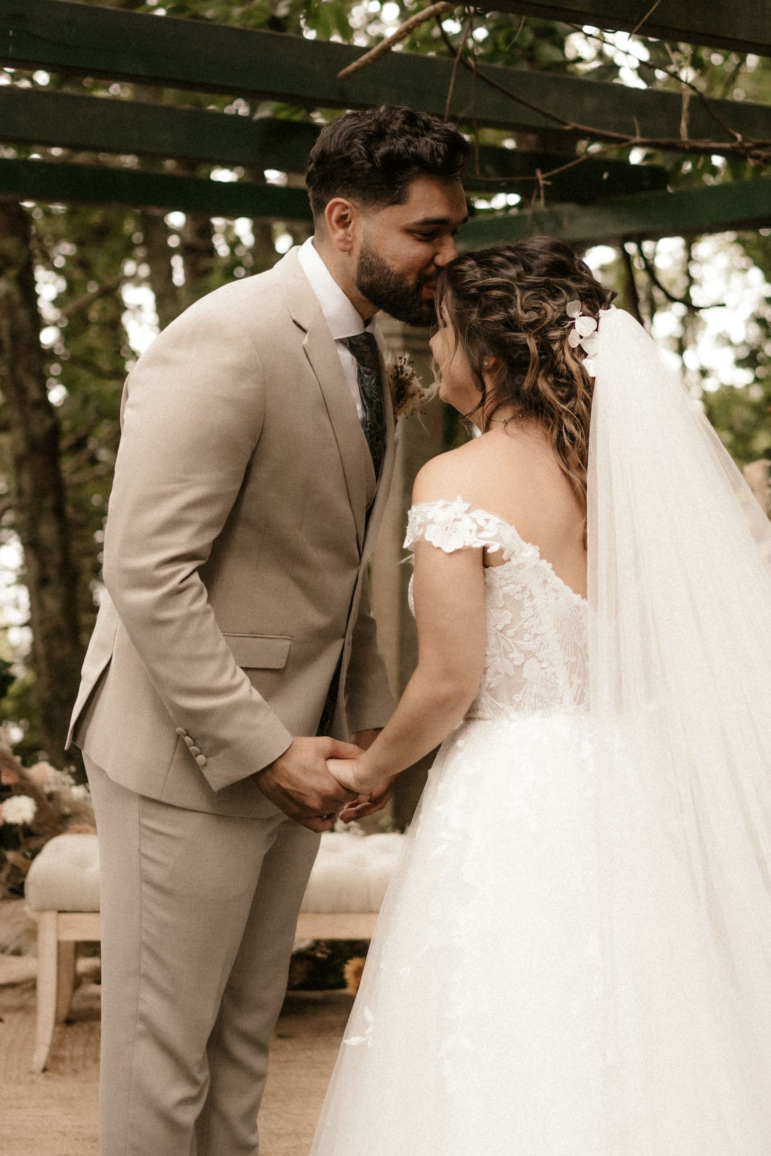 A couple shares an intimate first look moment at their outdoor wedding, with the bride in white and groom in beige.