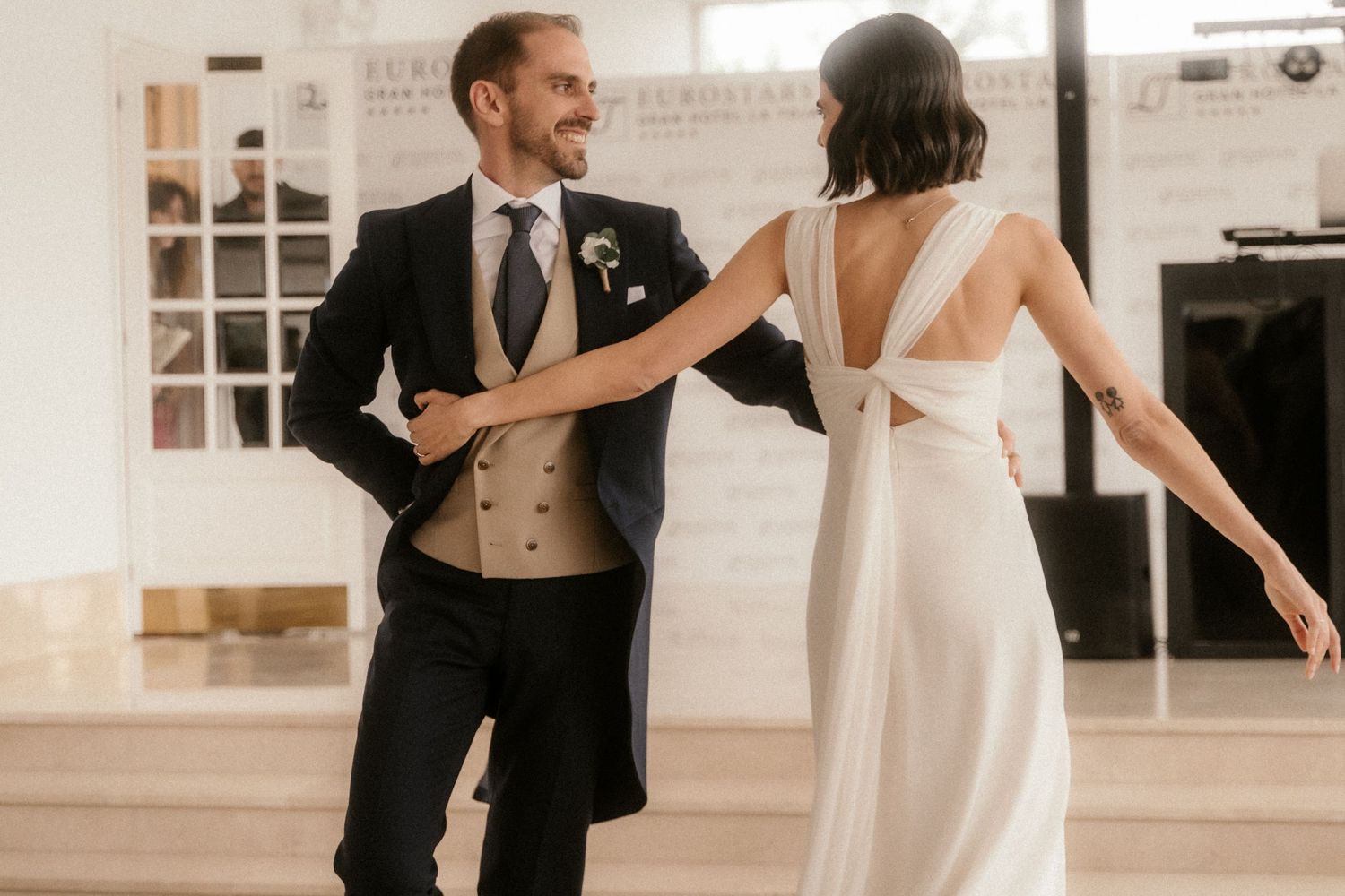 A couple dances together at their wedding reception, with the bride wearing a white backless gown and groom in dark suit.
