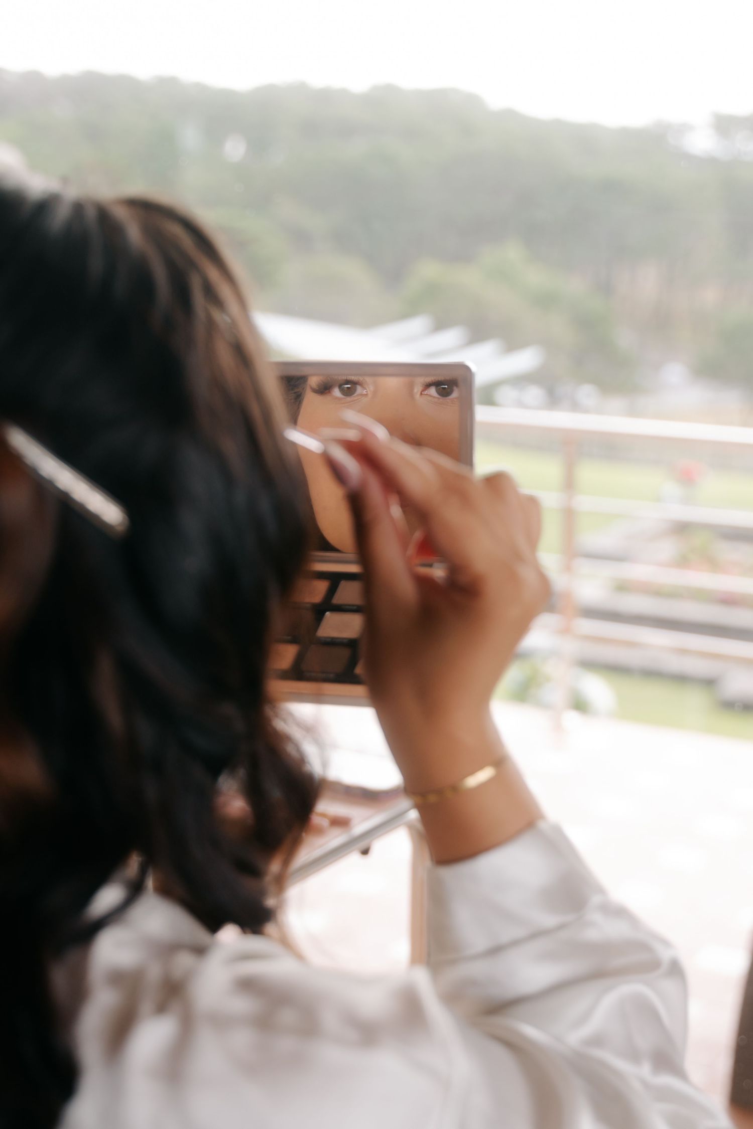 A person in a white sweater looking through a pair of binoculars against a blurred outdoor background.