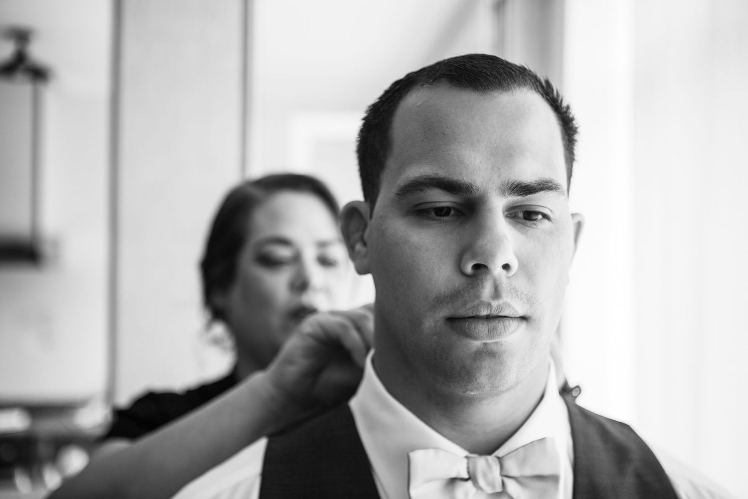 A series of black and white photos showing wedding preparation moments with a bowtie and formal attire.
