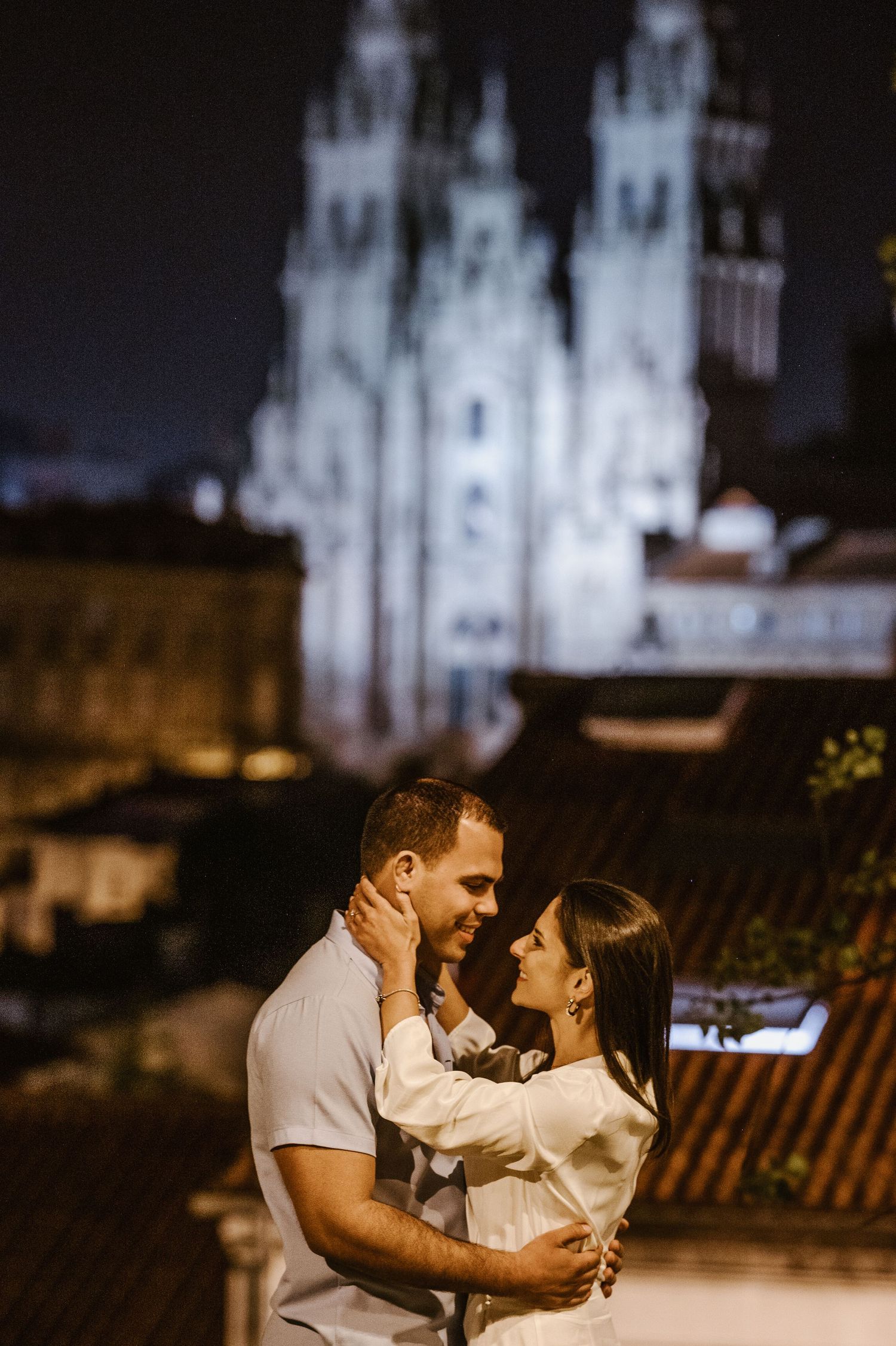 Romantic nighttime scene with couple embracing in front of illuminated Santiago de Compostela Cathedral in Spain.