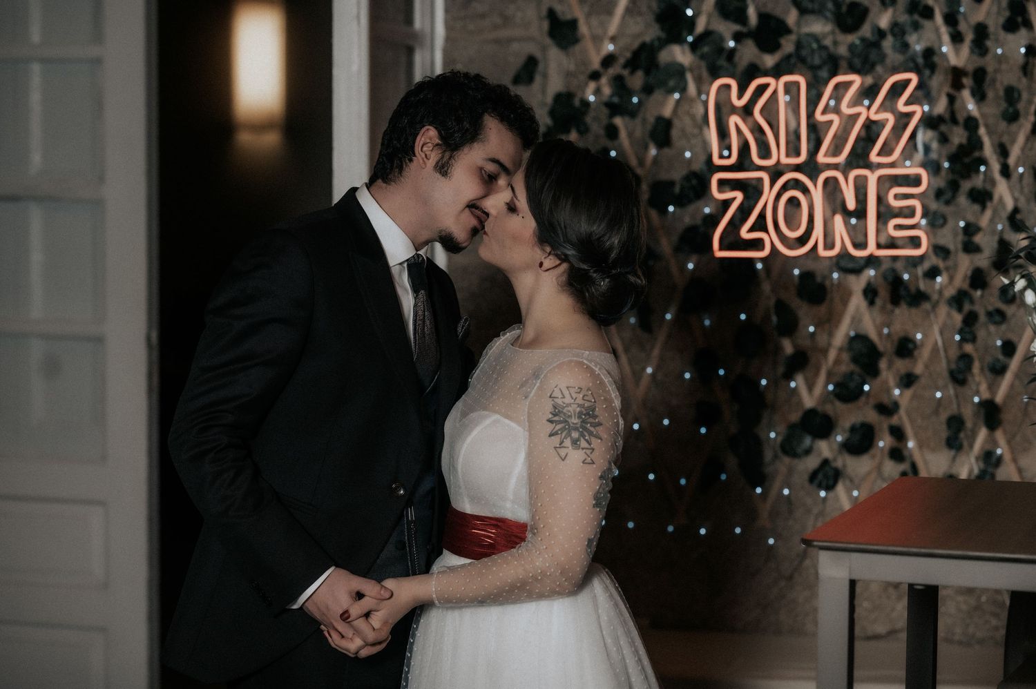 A couple shares a romantic kiss during their wedding celebration with sparkling lights in the background.