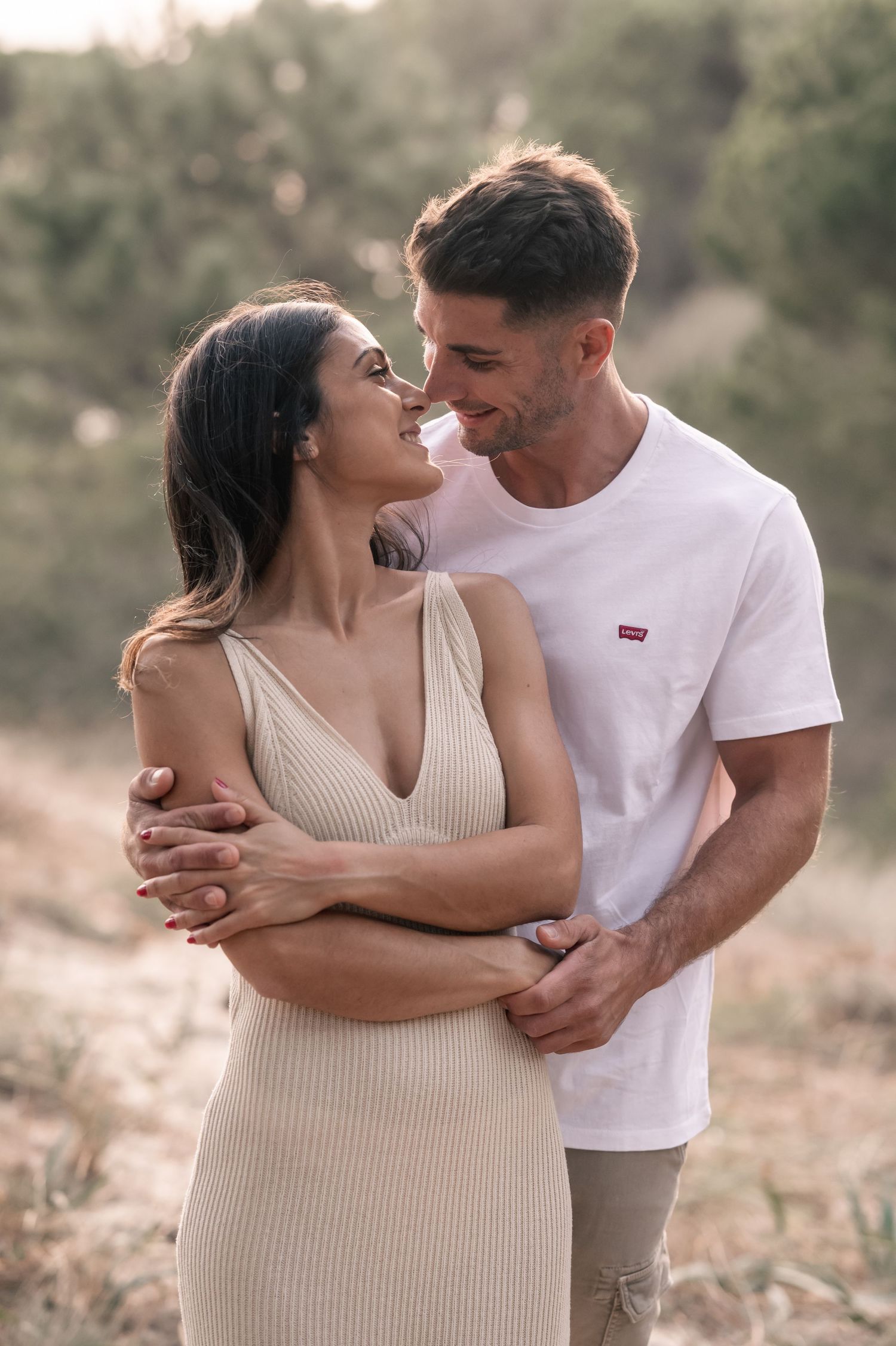 Intimate couple shares tender moments while embracing in casual attire against a natural backdrop.