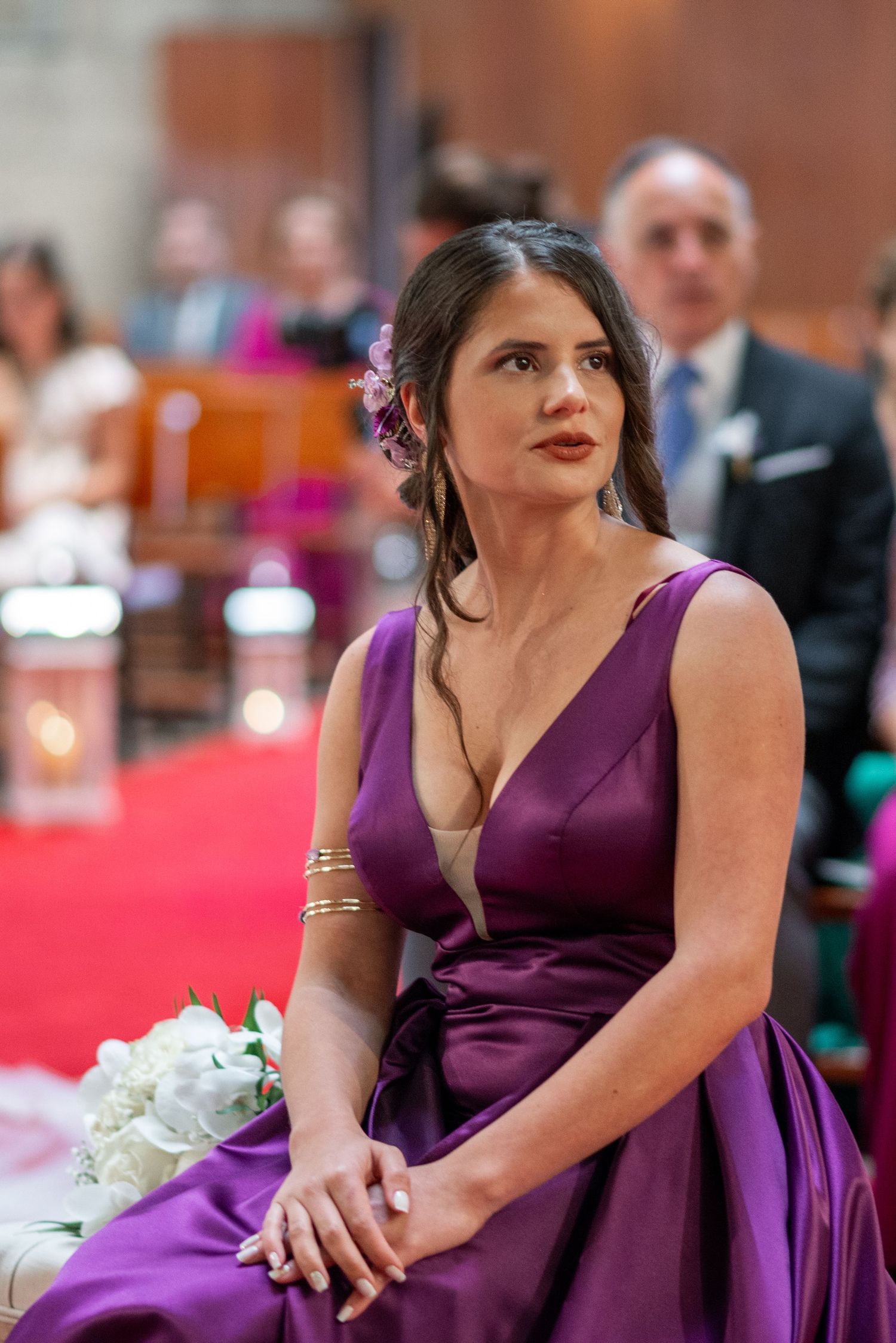 Bridesmaid in elegant purple dress holds white floral bouquet during wedding ceremony.