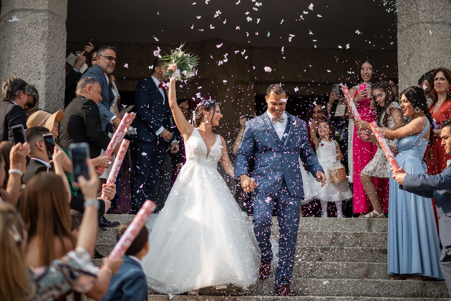 Wedding party celebration with confetti shower outside stone church entrance.