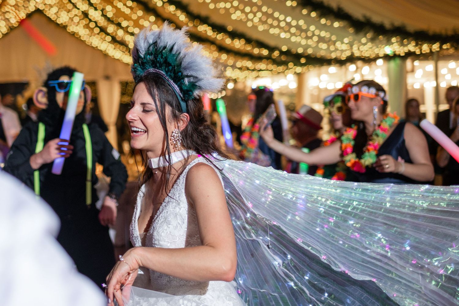 Wedding reception guests dance and celebrate under glowing string lights and decor.