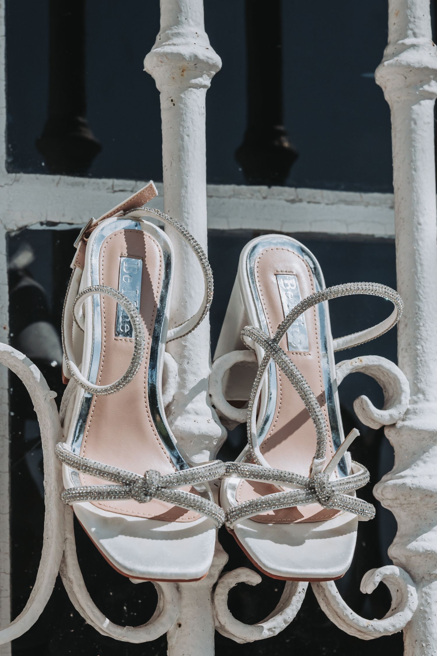 Elegant silver strappy bridal sandals displayed on ornate white railings.