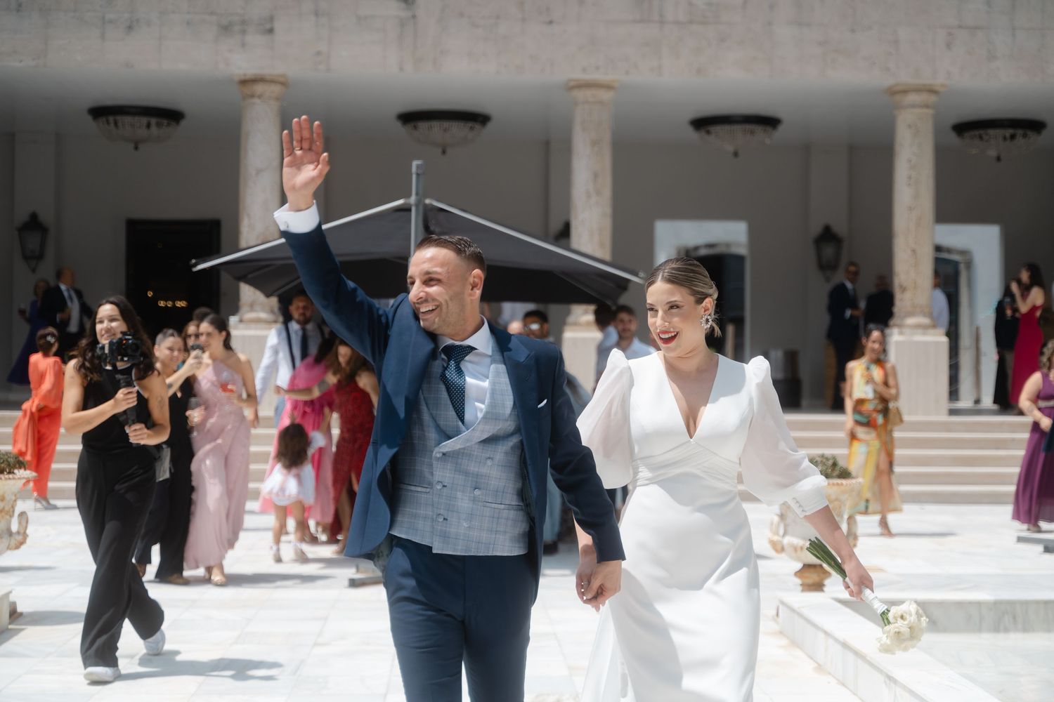 Wedding guests dancing and celebrating in an elegant columned venue with marble architecture.