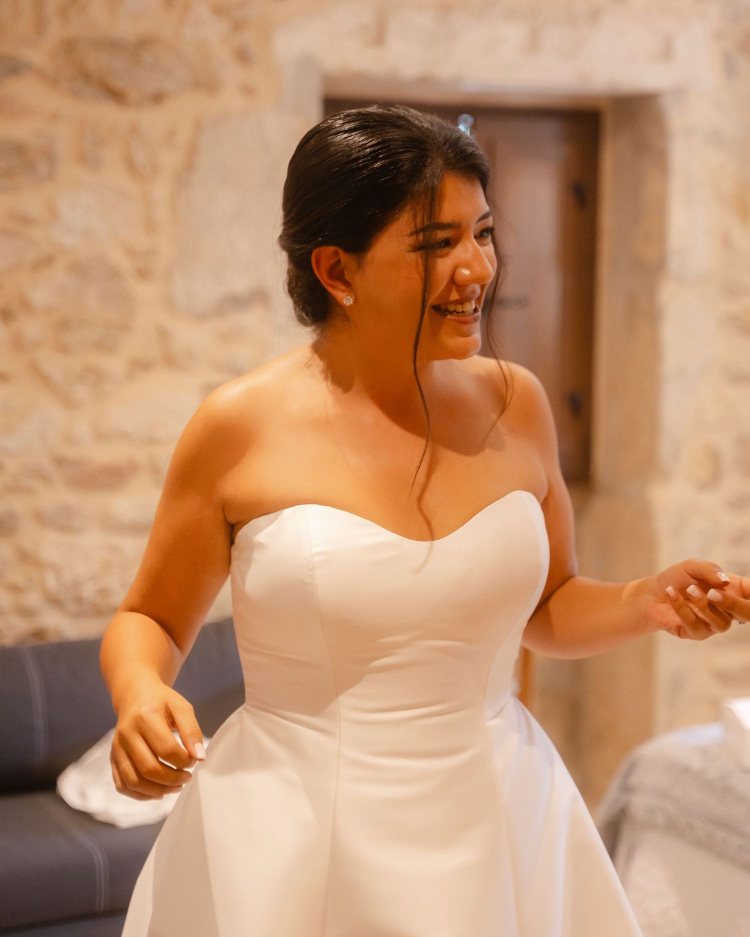 A bride in a strapless white wedding dress smiles while getting ready for her wedding day.