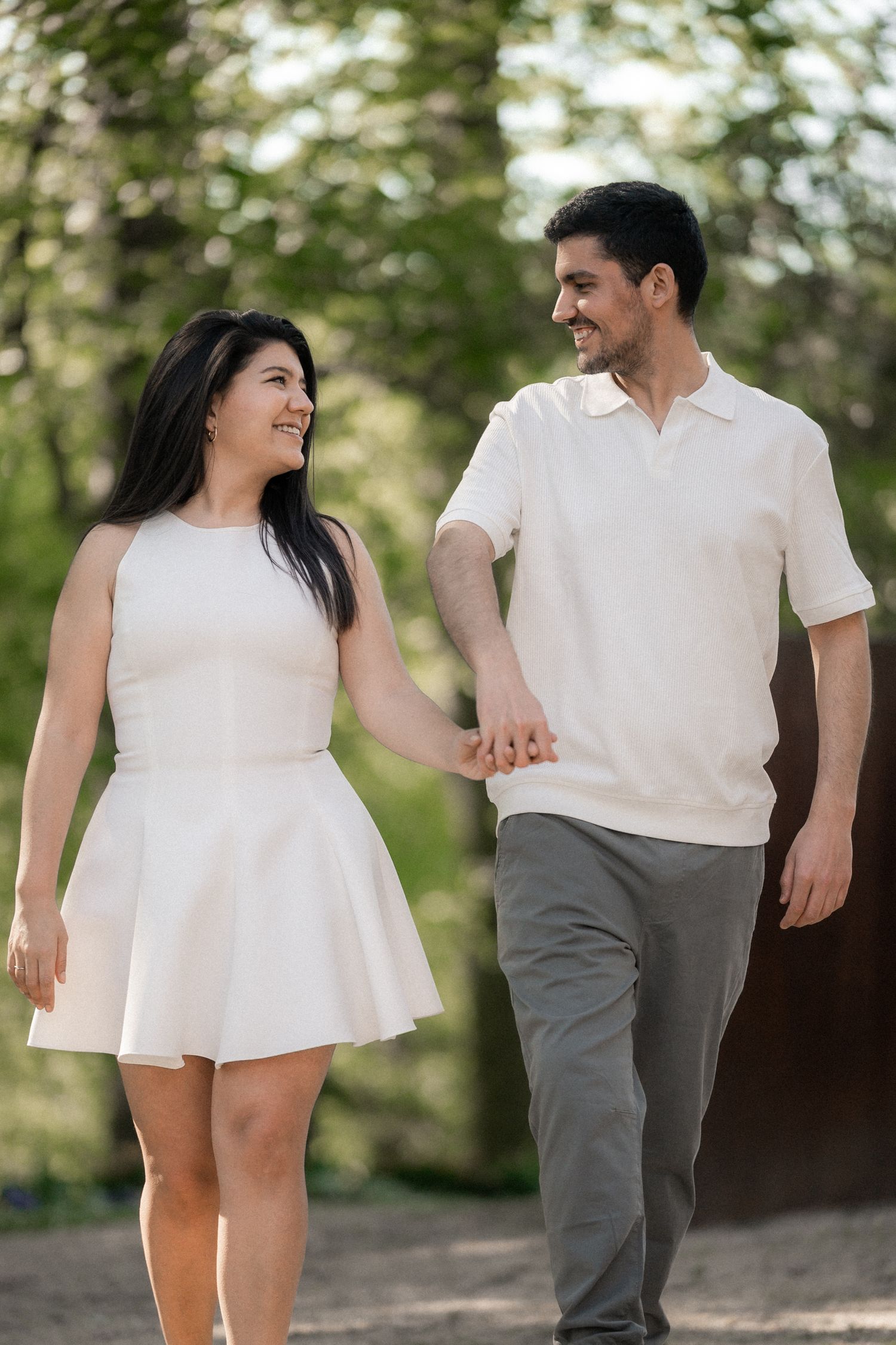 A couple in white and gray casual outfits share playful moments together during an outdoor photo session.