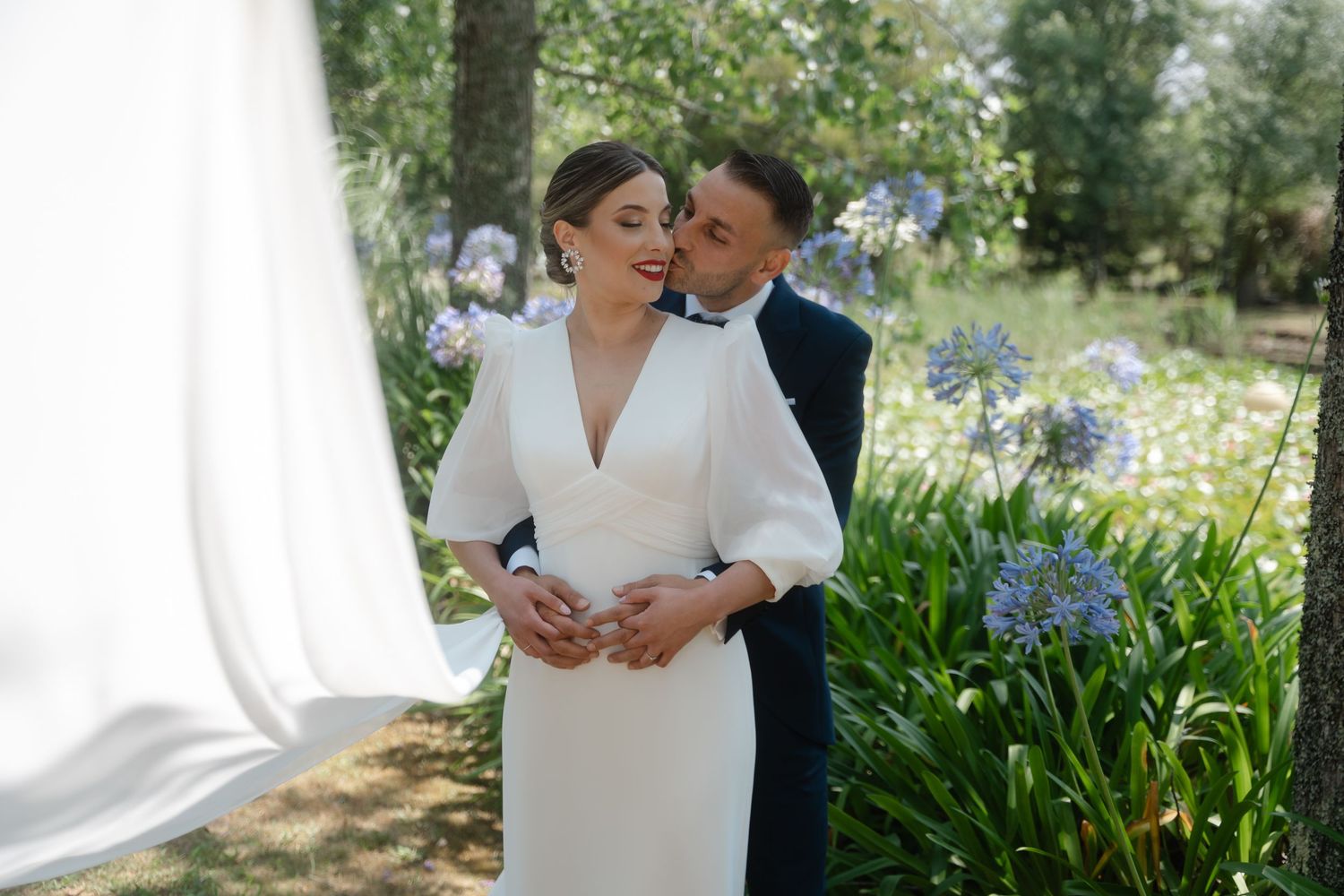 Romantic garden wedding portrait with couple embracing among blooming spring flowers.