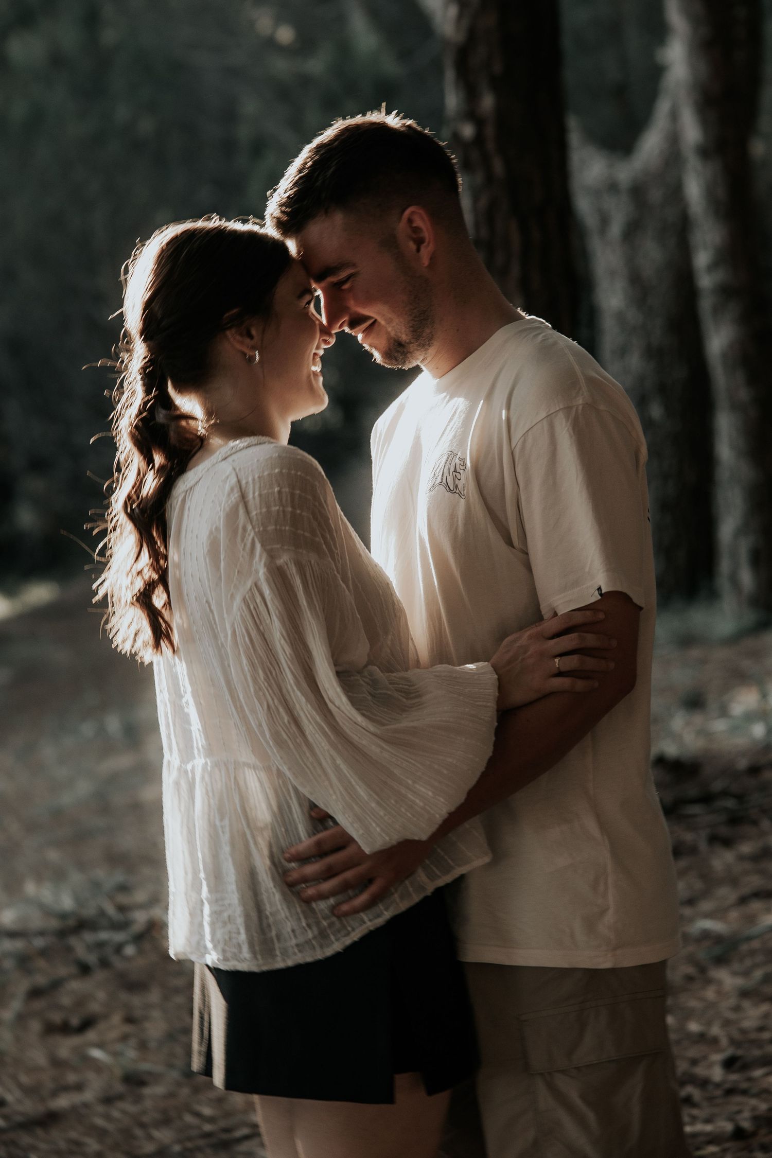 Romantic couple in white shirts share intimate moments in a moody forest setting with multiple poses.