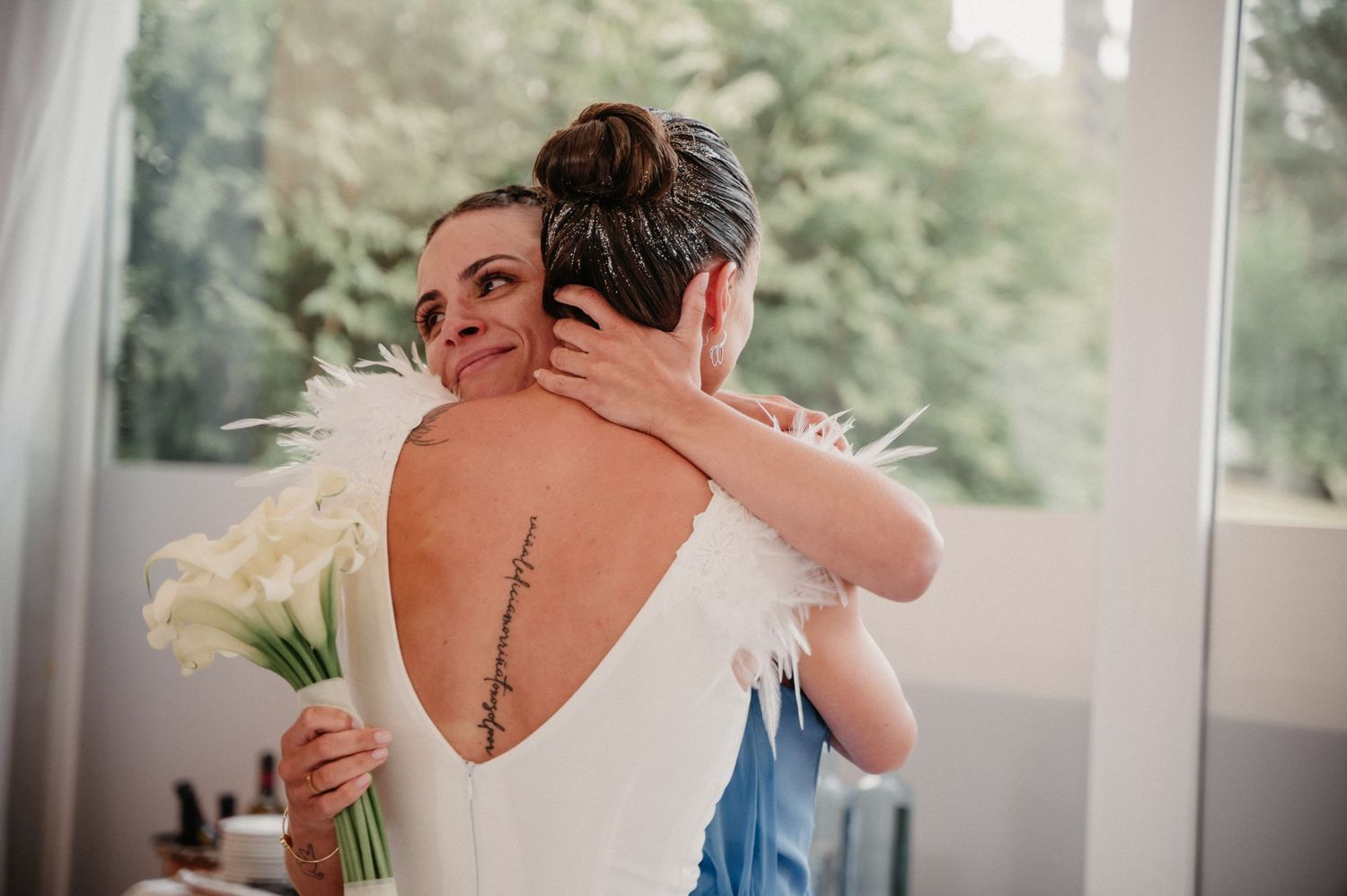 Two people embracing in a tender moment near large windows with natural light streaming in.