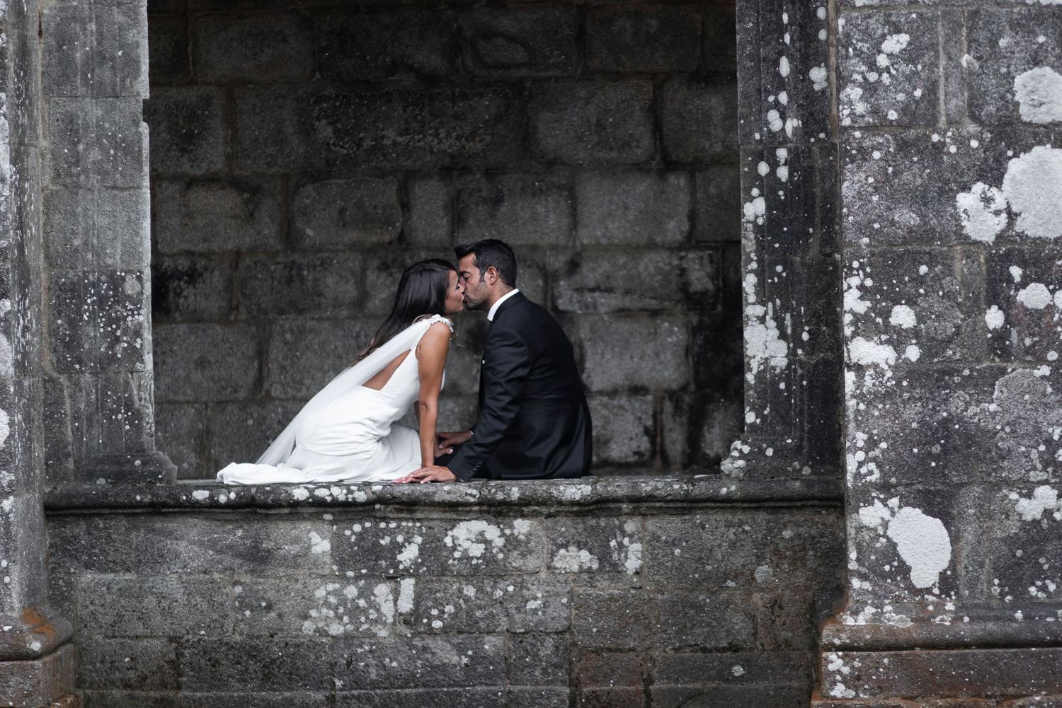 Black and white wedding portrait against textured stone wall architecture.