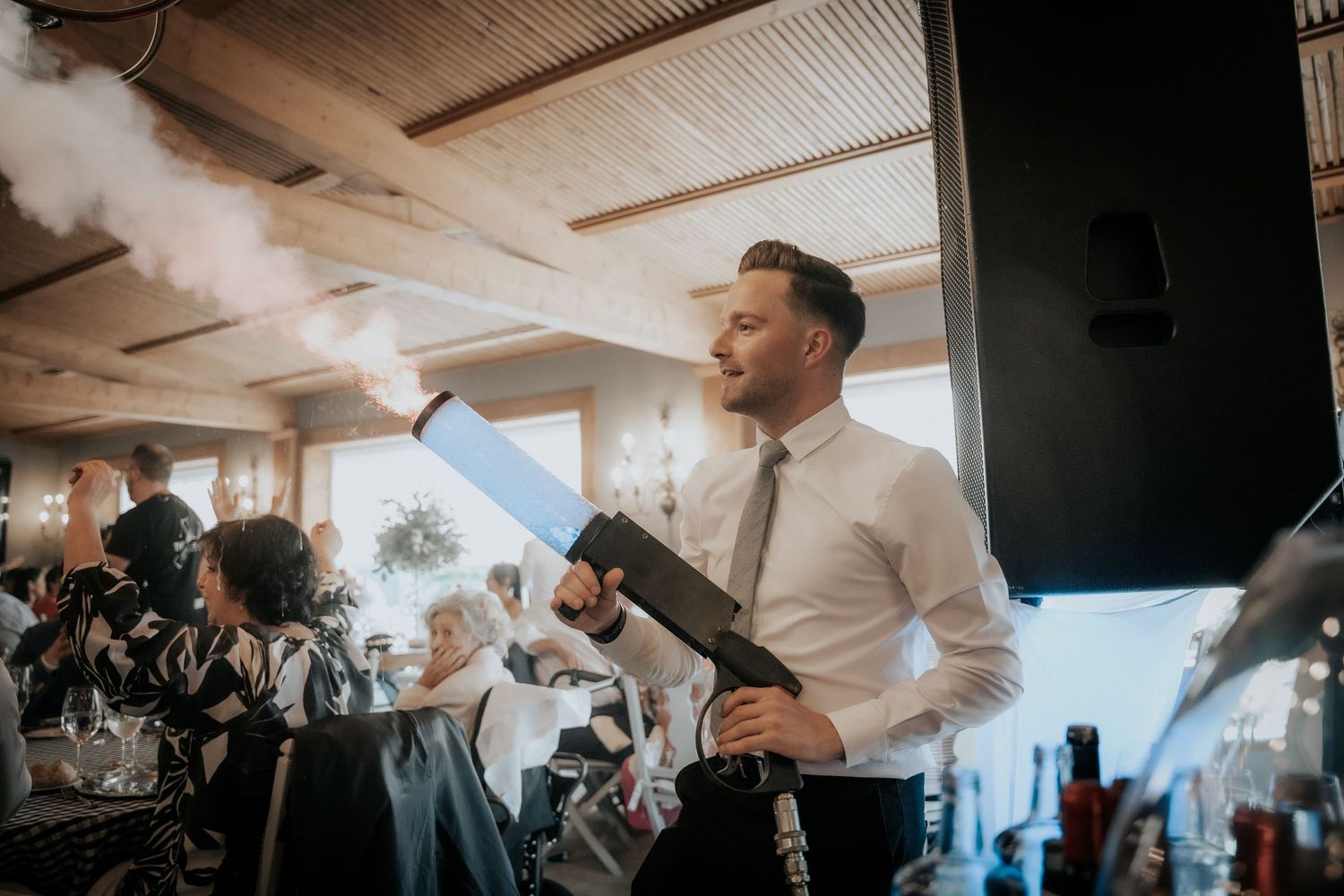 People dancing and celebrating at an indoor wedding reception with warm lighting and wooden beams.