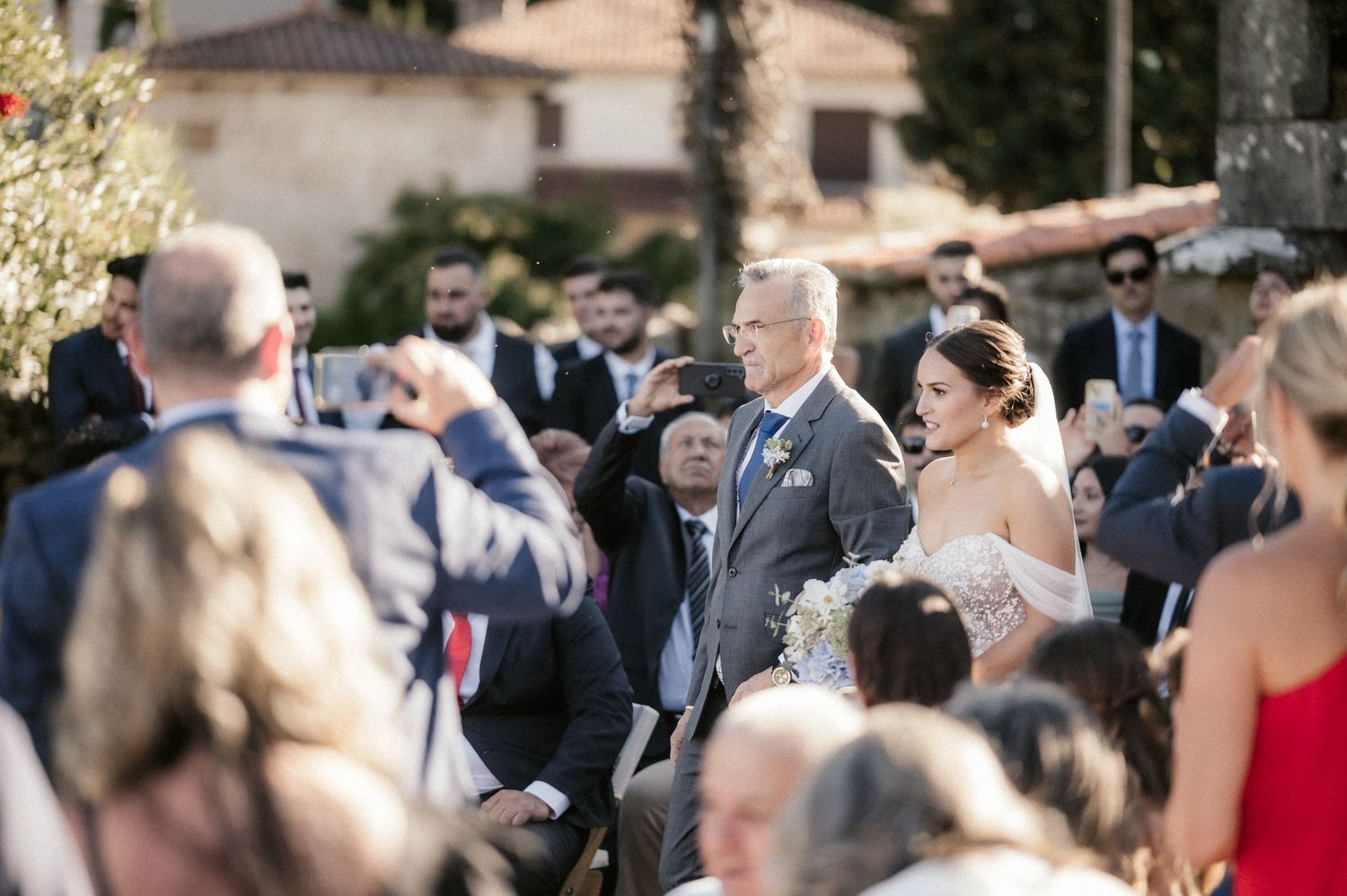 A group of wedding guests mingle and socialize during an outdoor cocktail reception on a sunny afternoon.