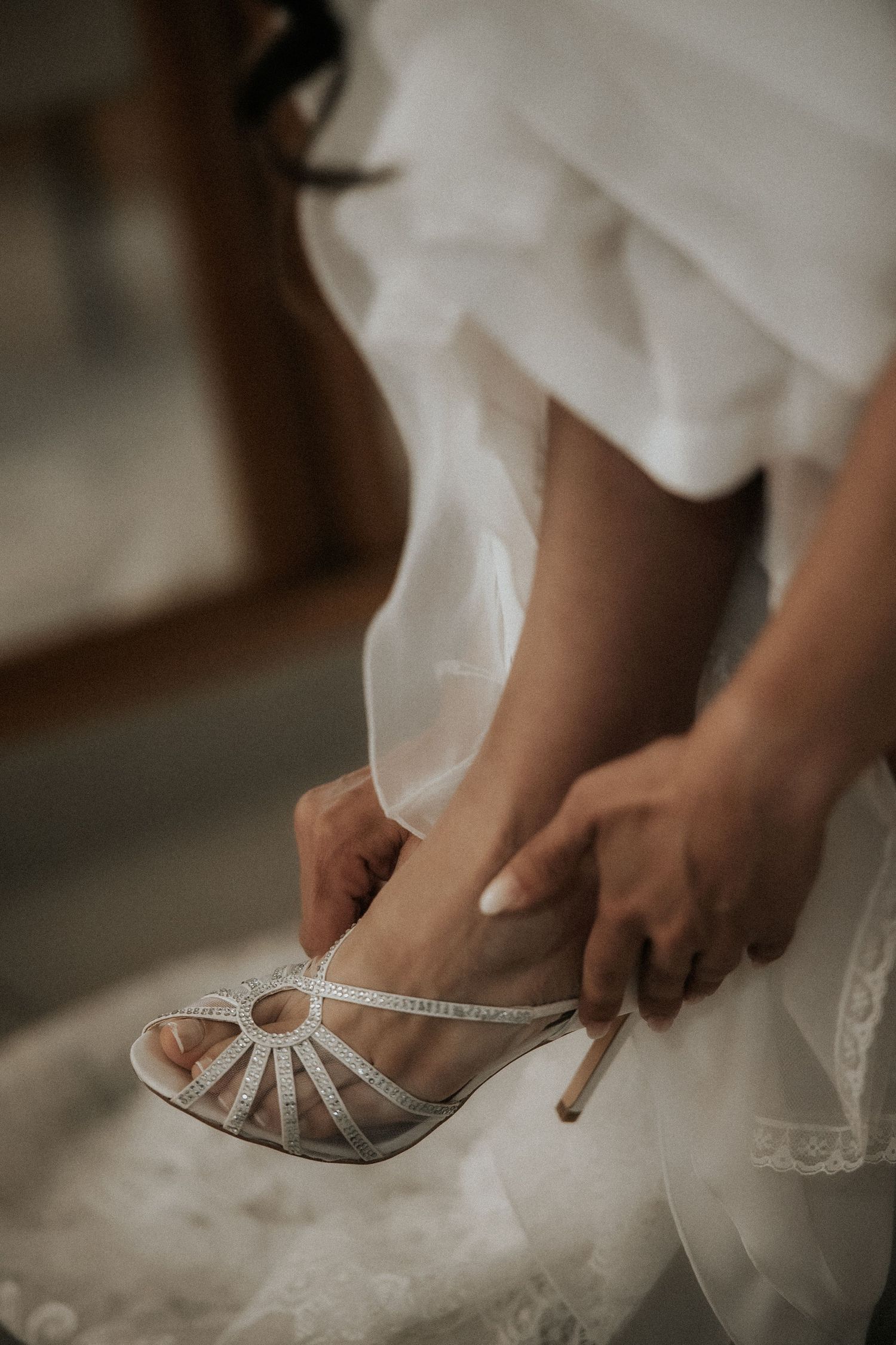 Close-up of a sparkly silver bridal shoe being put on with white dress fabric flowing around it.