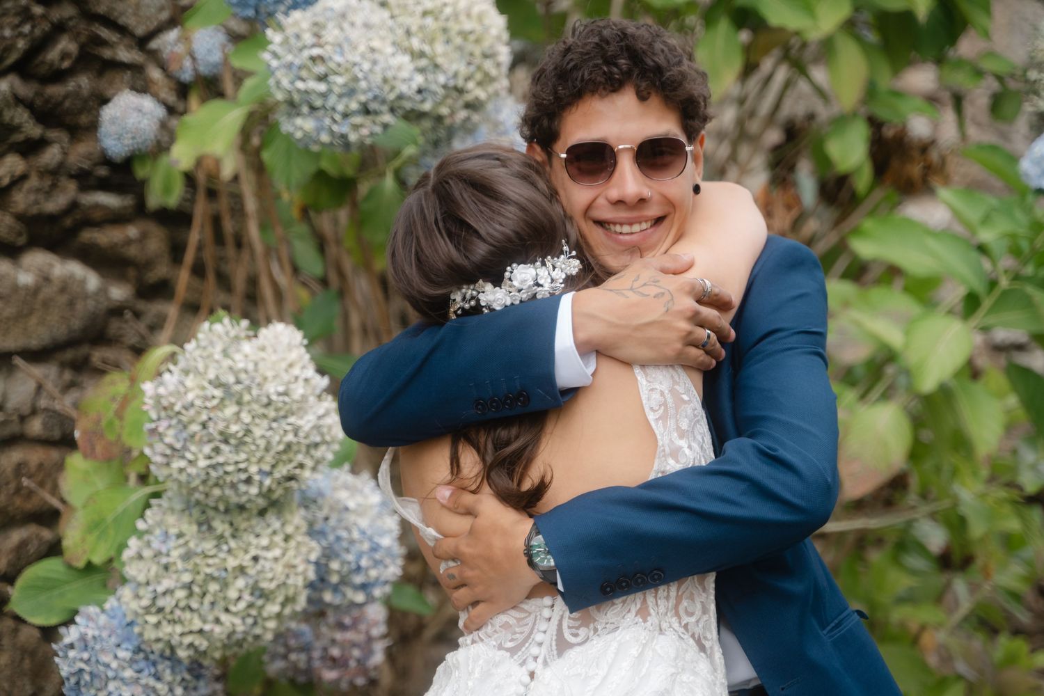 A couple shares an emotional embrace outdoors surrounded by greenery and baby's breath floral decorations.