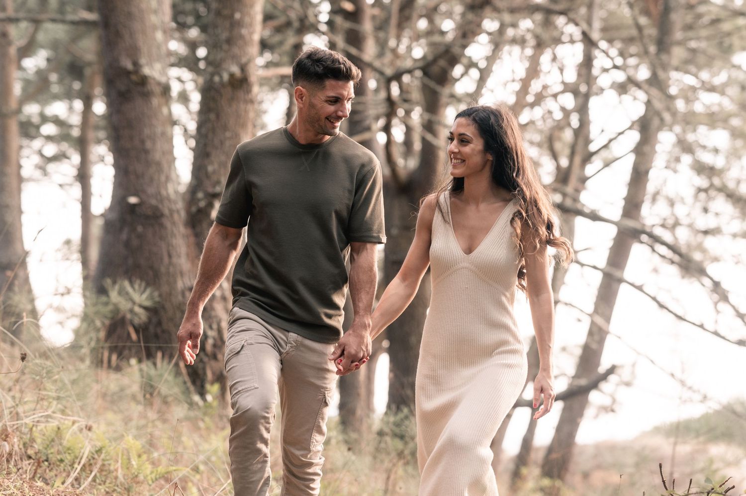 A couple walking hand in hand through a misty forest path wearing casual summer attire.